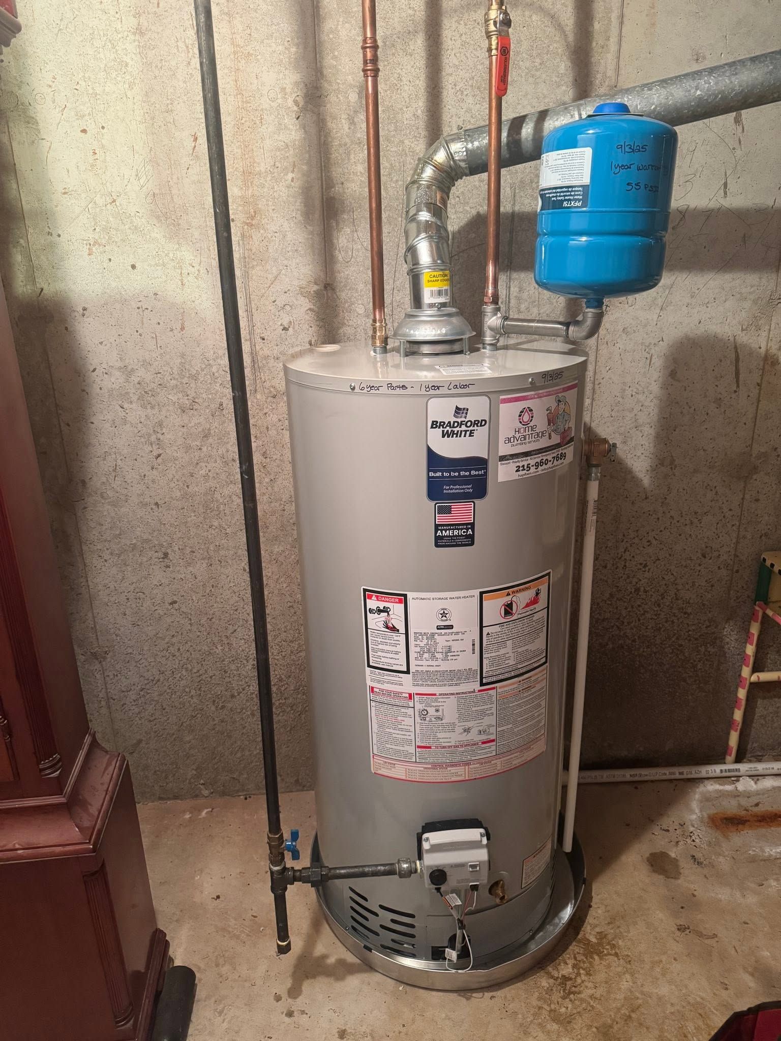 Water heater with a blue expansion tank and pipes in a utility room, against a concrete wall.