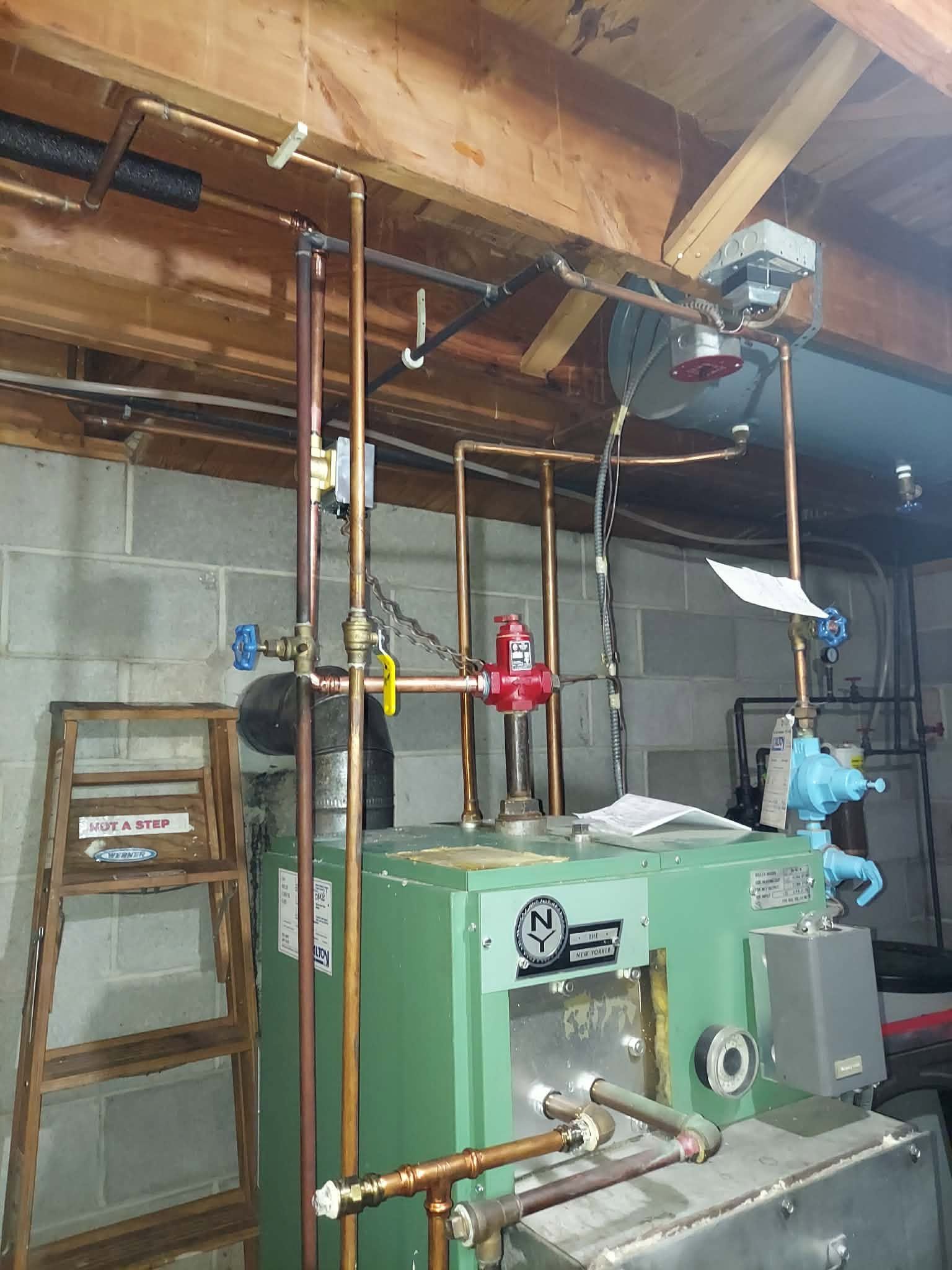 Basement utility room with green boiler, copper pipes, red valve, and exposed ceiling beams