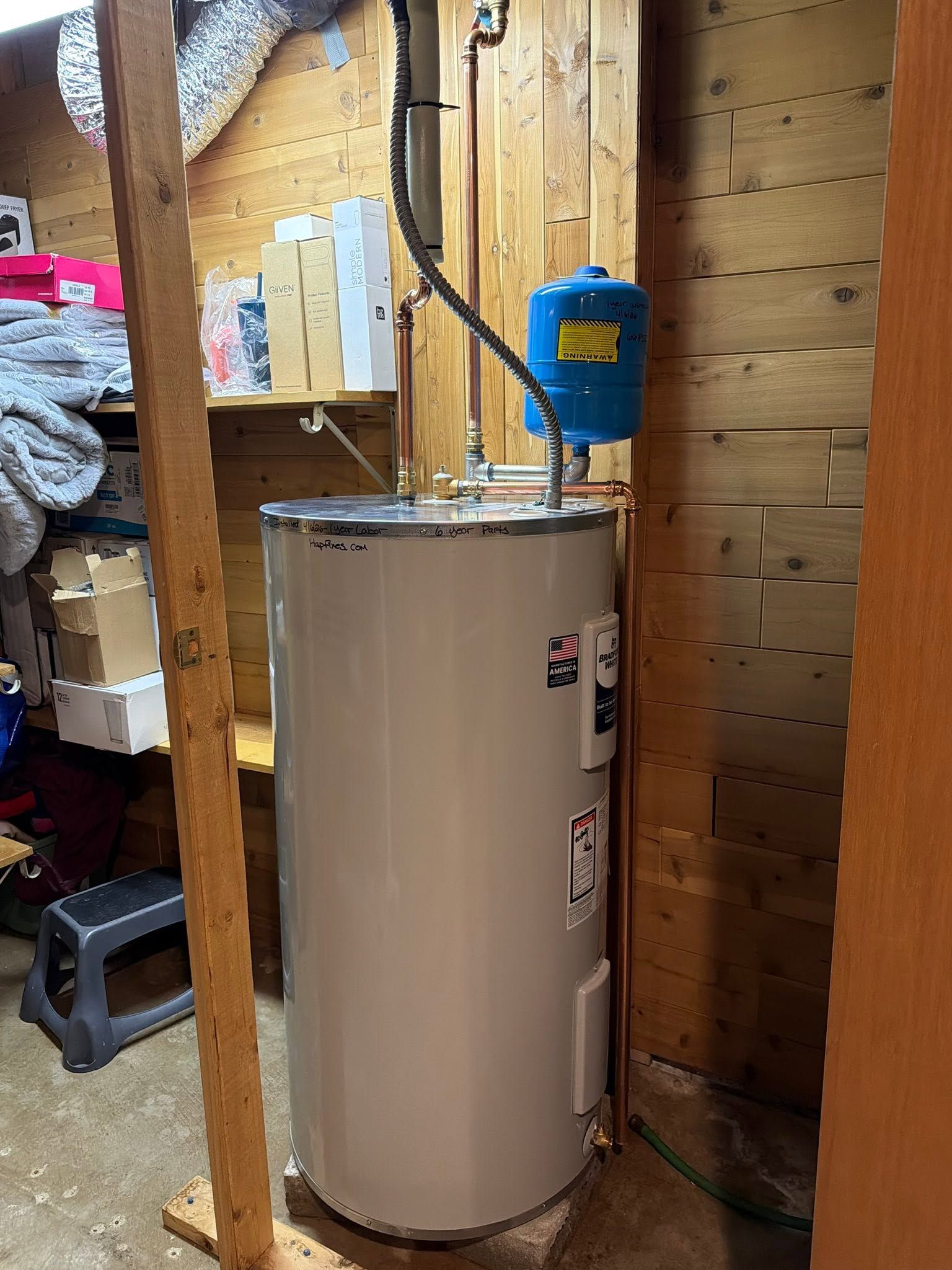 Water heater in a utility room beside wooden framing and a blue wall-mounted device.