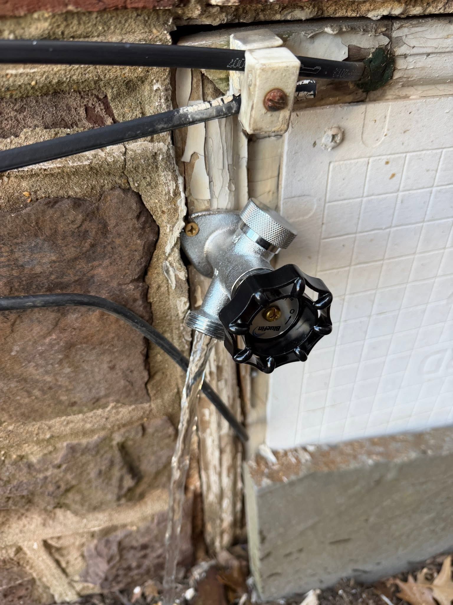 Broken outdoor wall outlet with exposed black wires and damaged white conduit beside a tiled wall