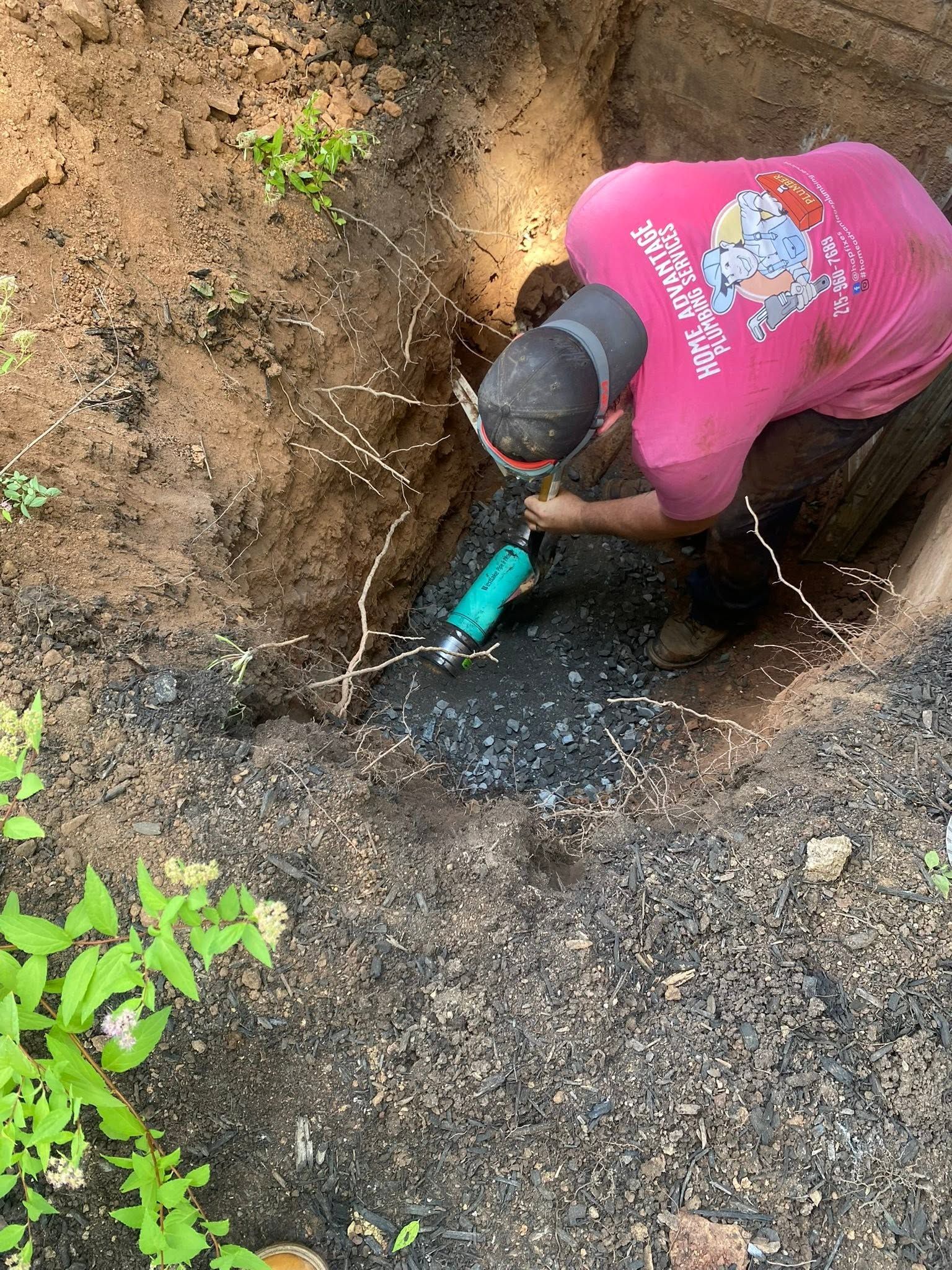 Person in a pink shirt digging in a muddy hole with a small green tool outdoors