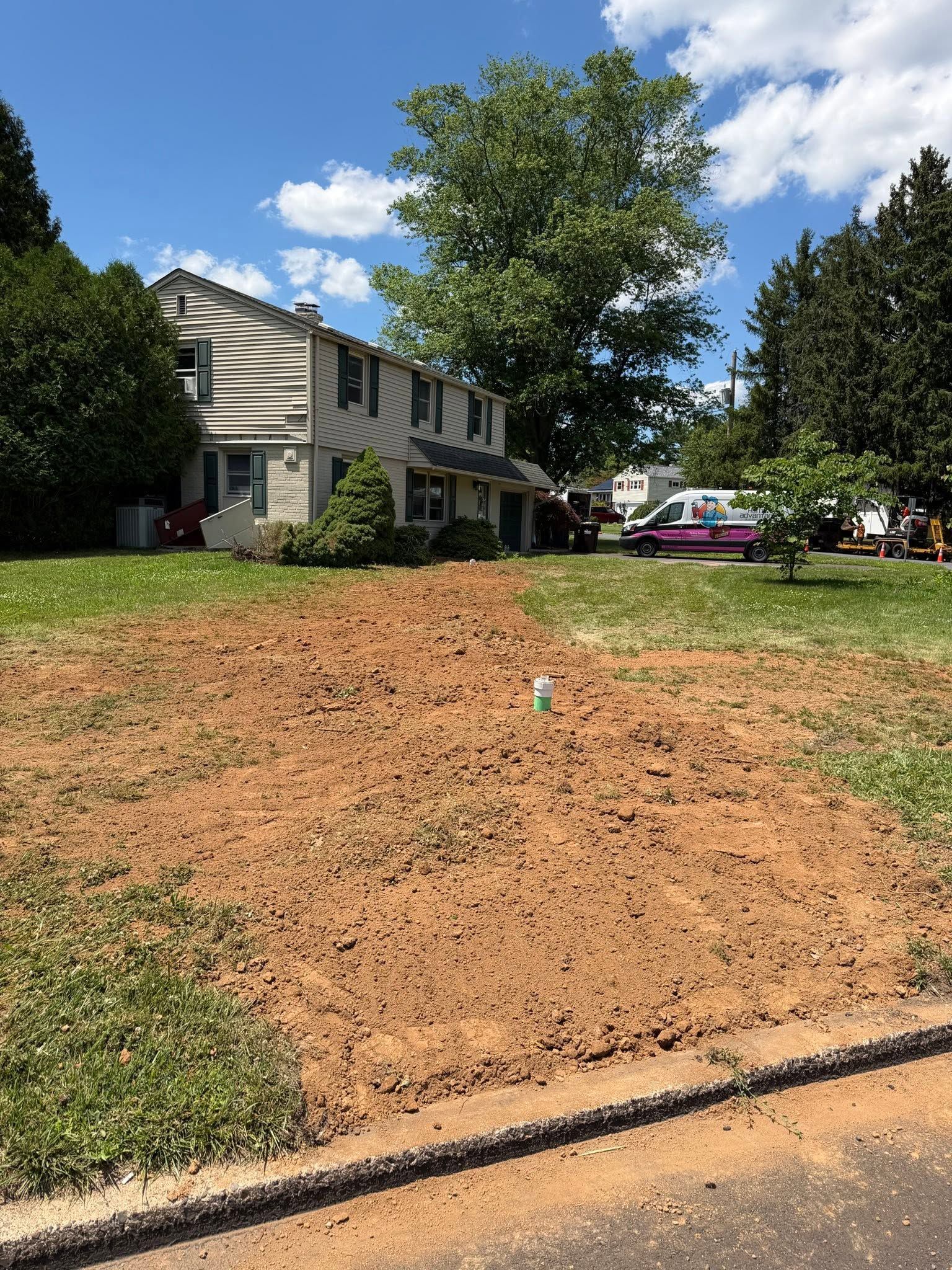 Front yard with bare dirt patch, suburban house, and a white car under a blue sky