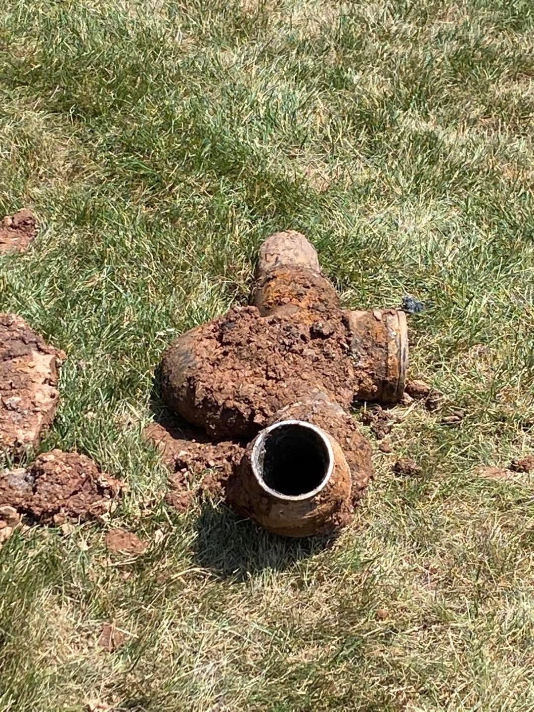 Rusty broken pipe or sprinkler head in a grassy lawn with a clump of dirt around it