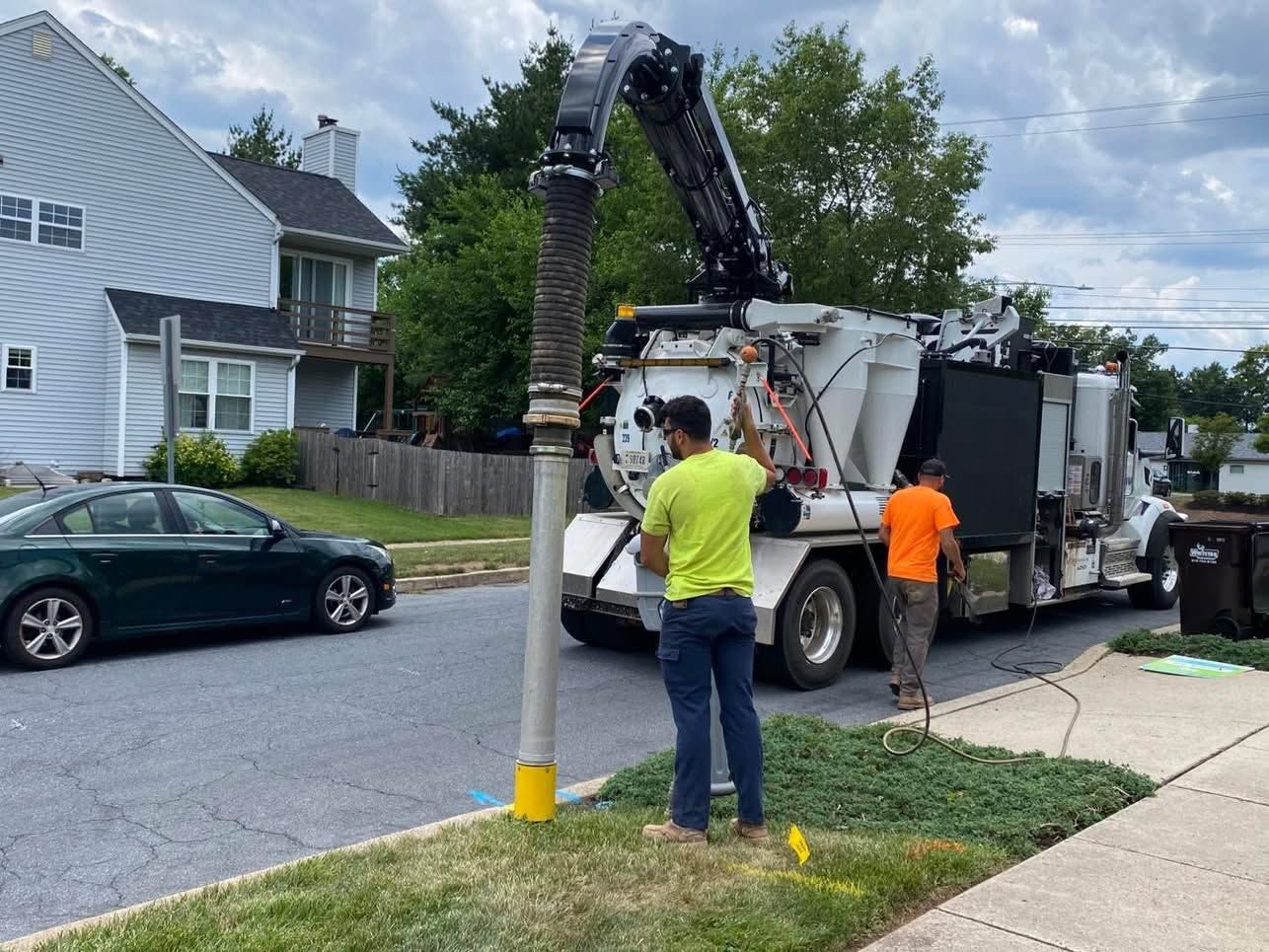 Street-cleaning truck vacuuming a sewer line, with two workers on a residential street.