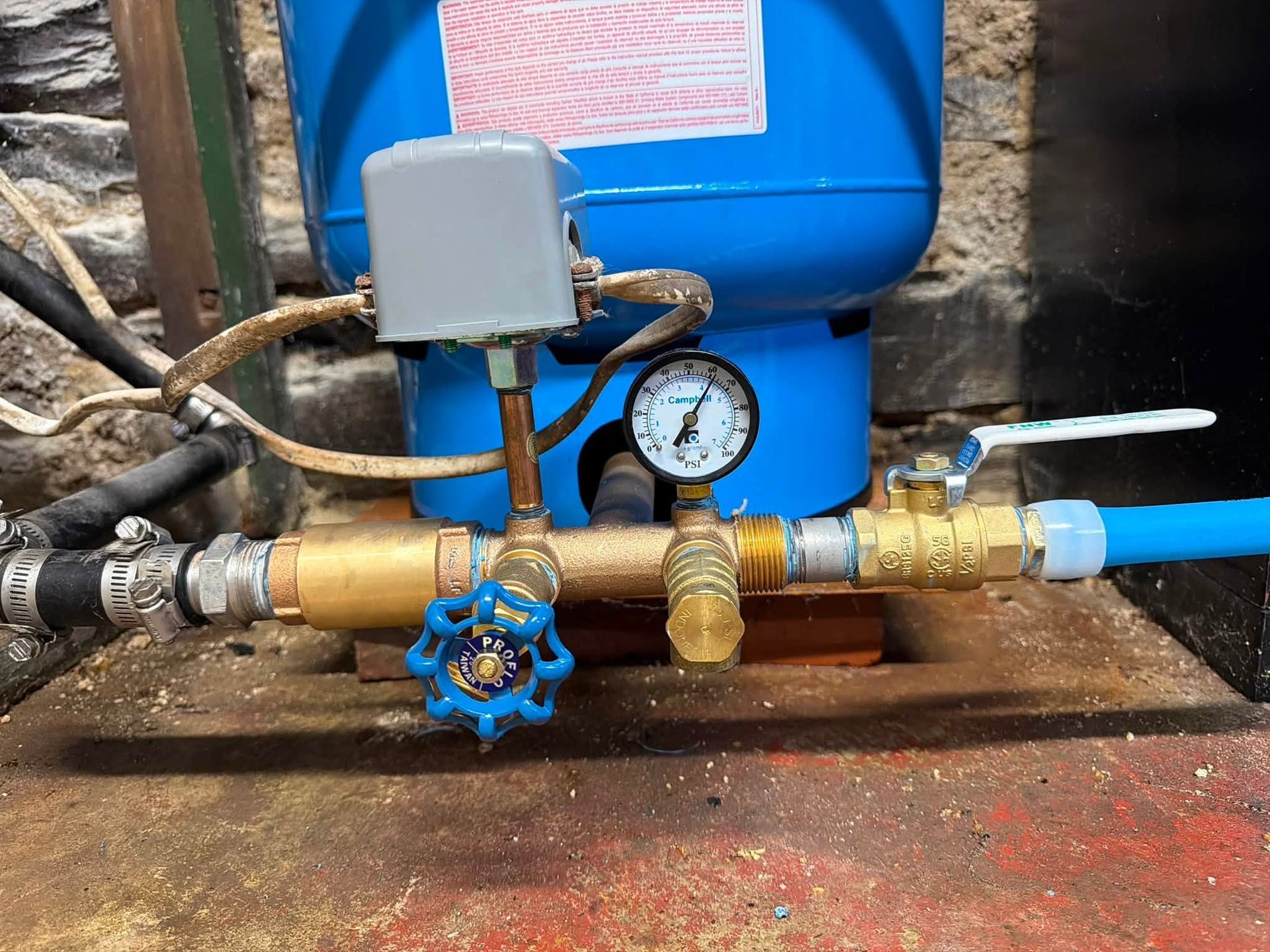 Blue water tank with pressure gauge, valves, and pipes in a utility setup