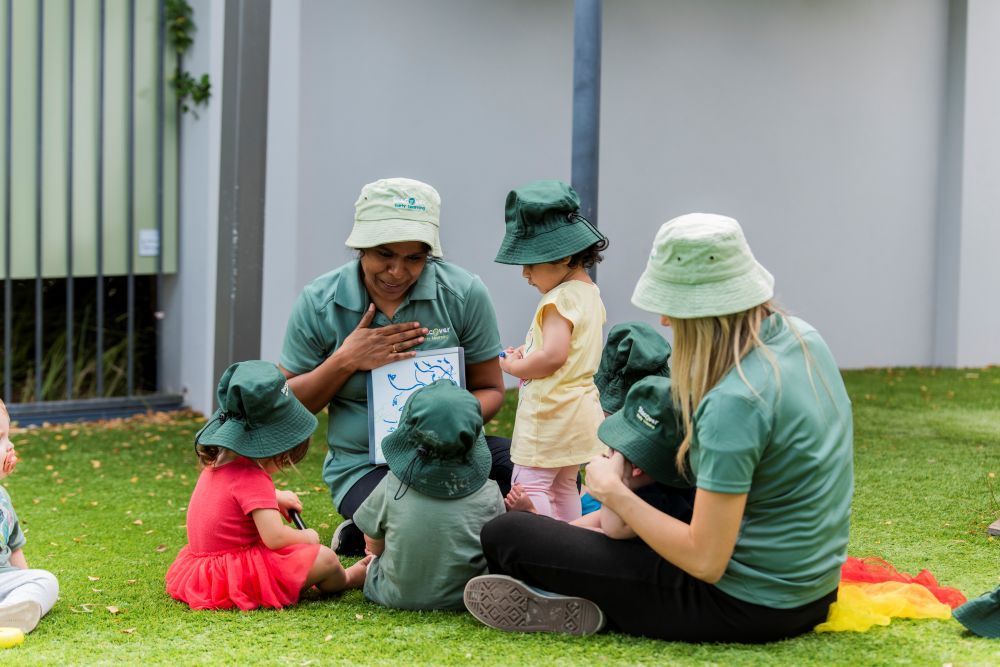 A group of children are sitting on the grass with a teacher at Discover Early Learning.