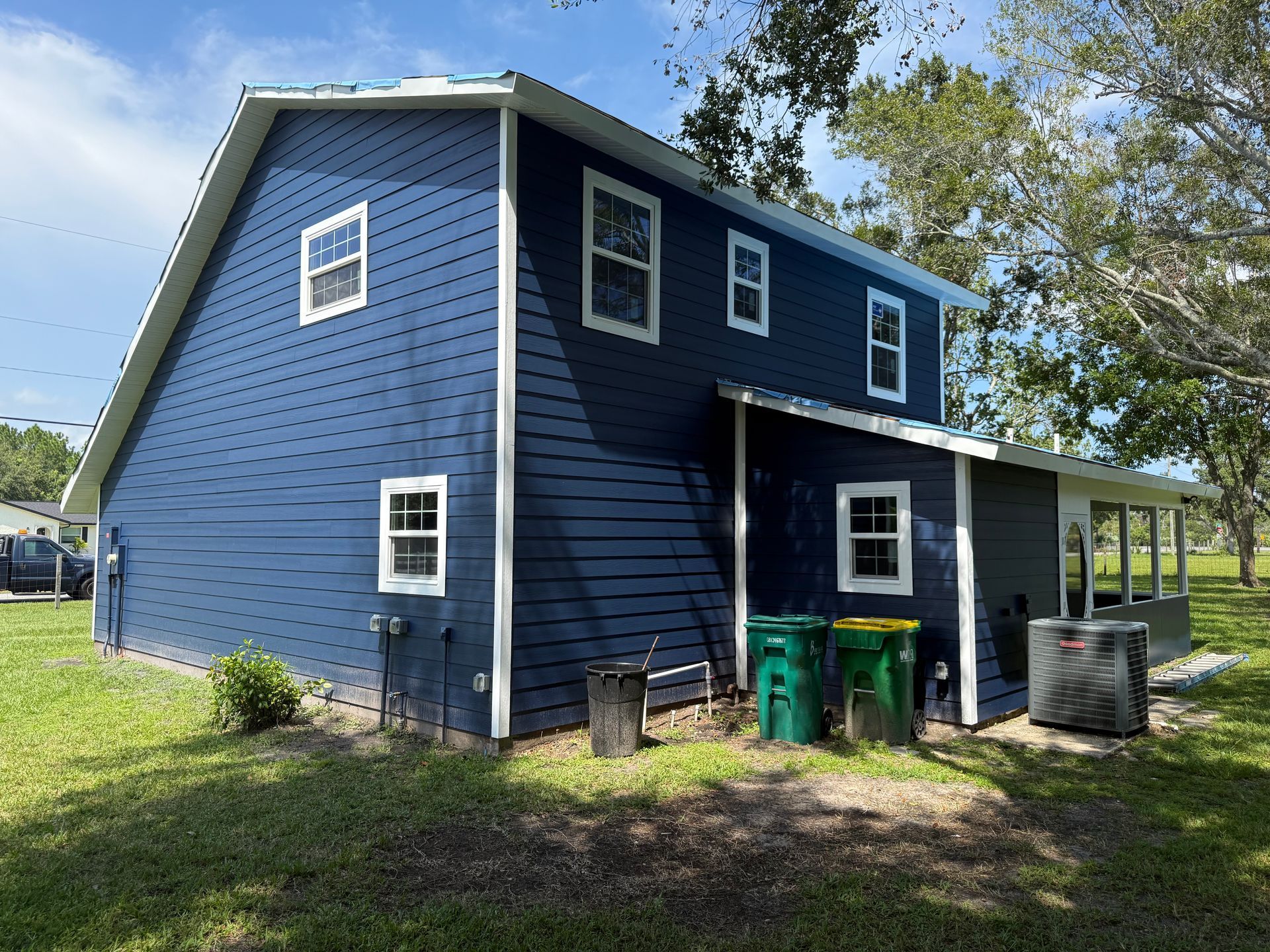 Blue house with white trim, green yard, and trash cans.