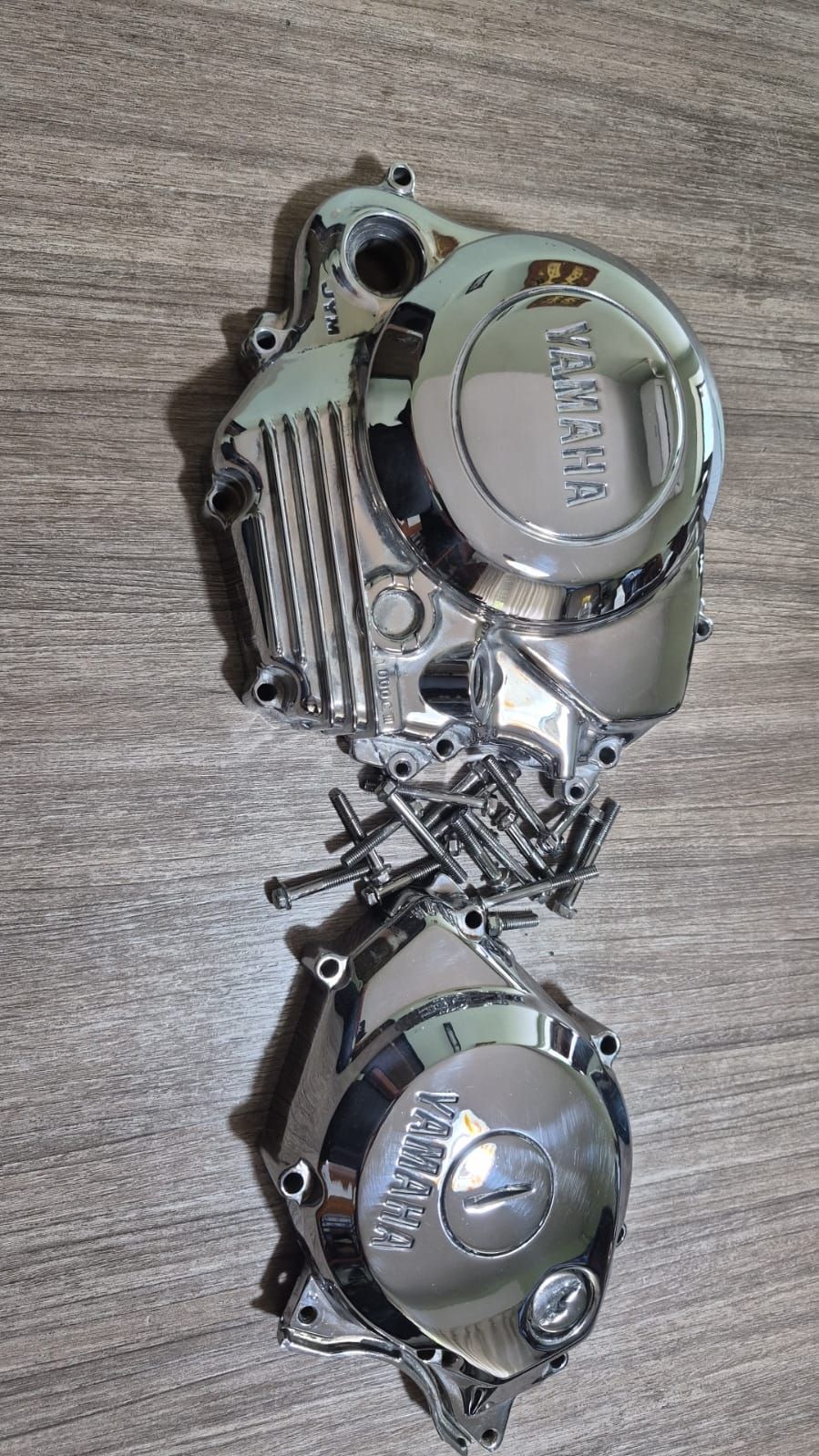 Dos tapas plateadas de relojes de pulsera unidas por una cadena retorcida sobre una superficie de madera