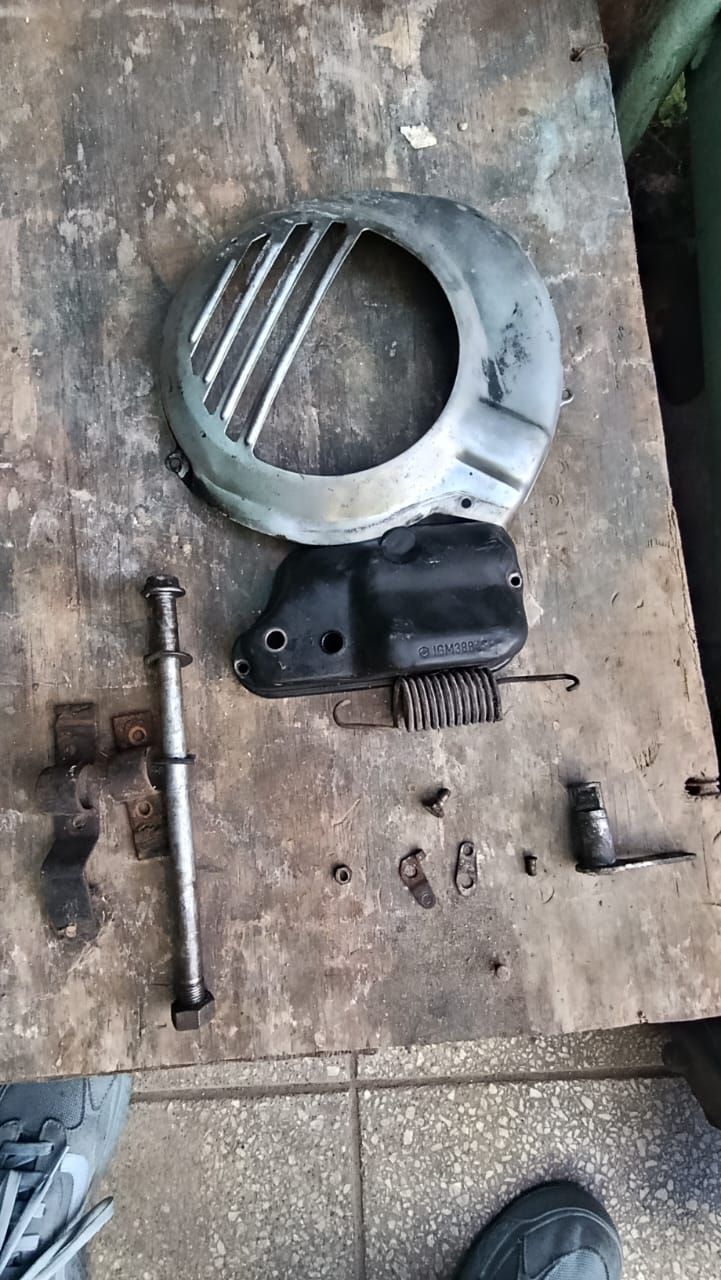 Piezas metálicas desmontadas de una máquina y herramientas sobre el suelo de un banco de trabajo desgastado.
