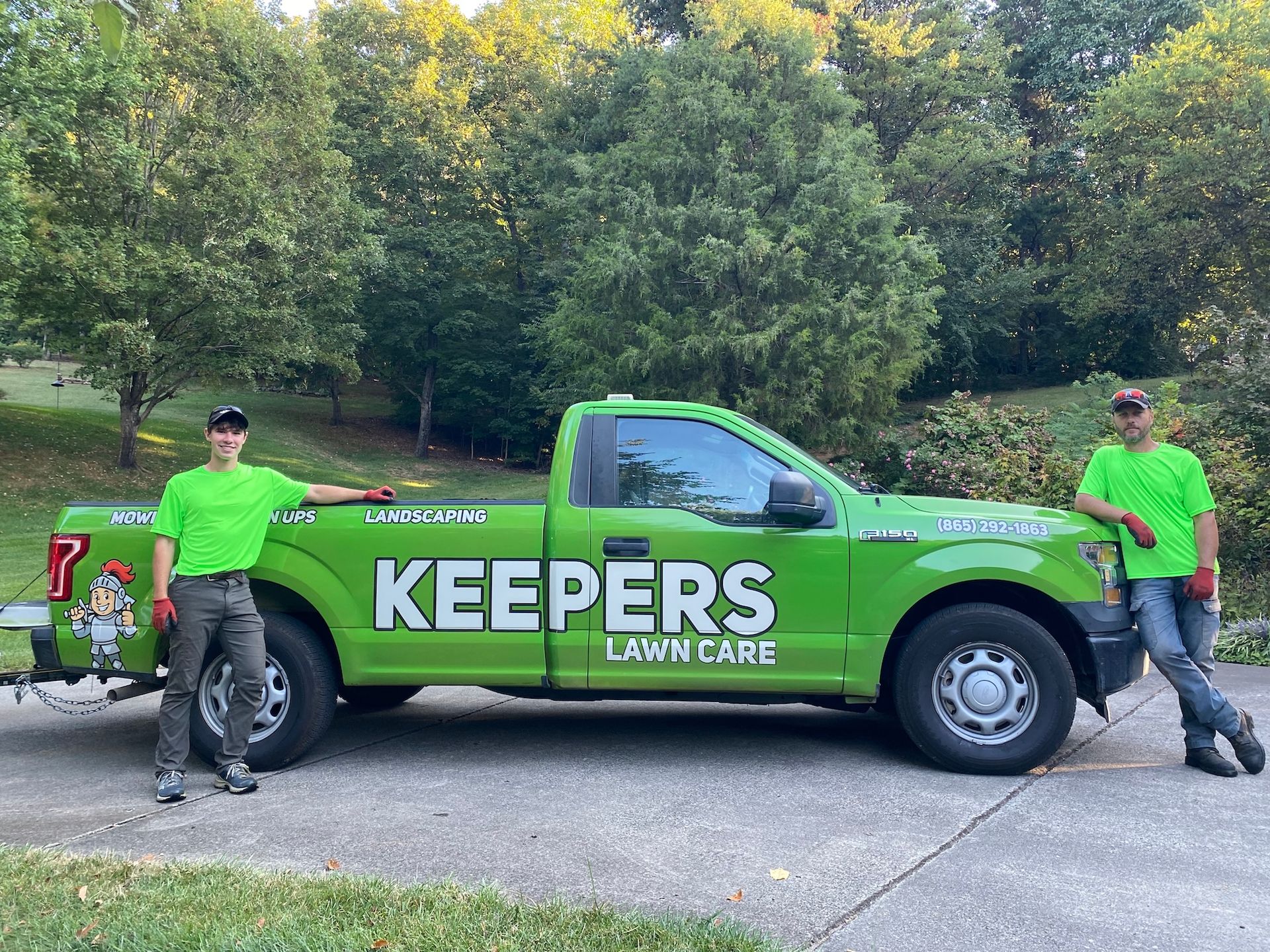 Two men in green shirts stand by a green truck that says 