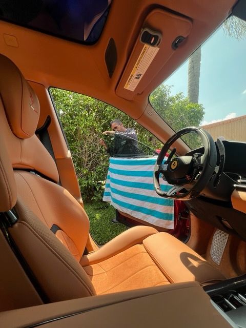 Tan leather interior of a red Ferrari. Person leans against the car, a striped towel draped across the open door.
