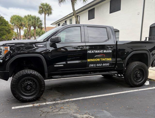 Black pickup truck with tinted windows, parked in a parking lot. It has a company logo on the side.