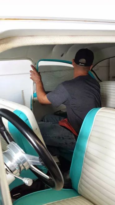 Man working on interior of a classic car, light blue and white upholstery.