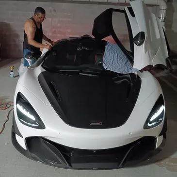 Man working on white and black McLaren sports car with doors open.