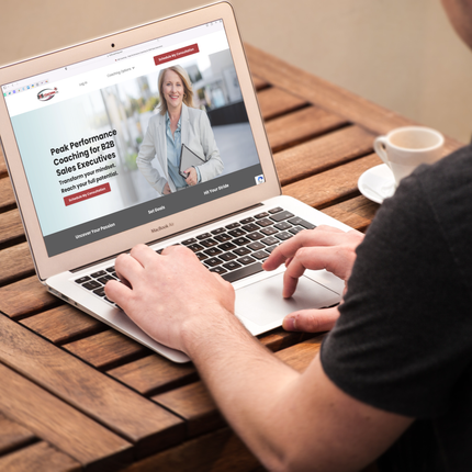 close up of man's hand typing on a laptop with website homepage showing smiling blonde woman on the screen