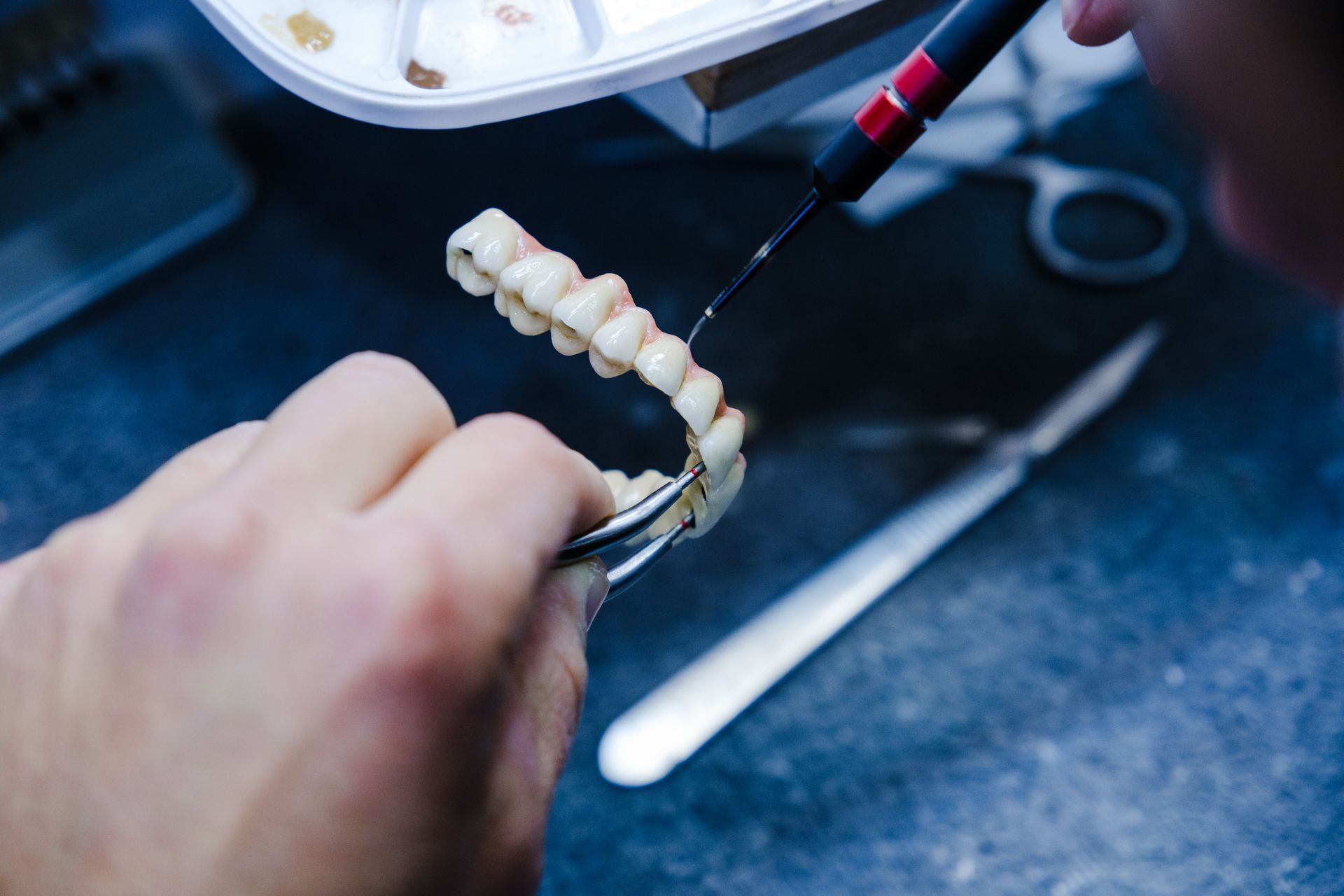 Close-up of a dentist performing denture repairs using a tool.