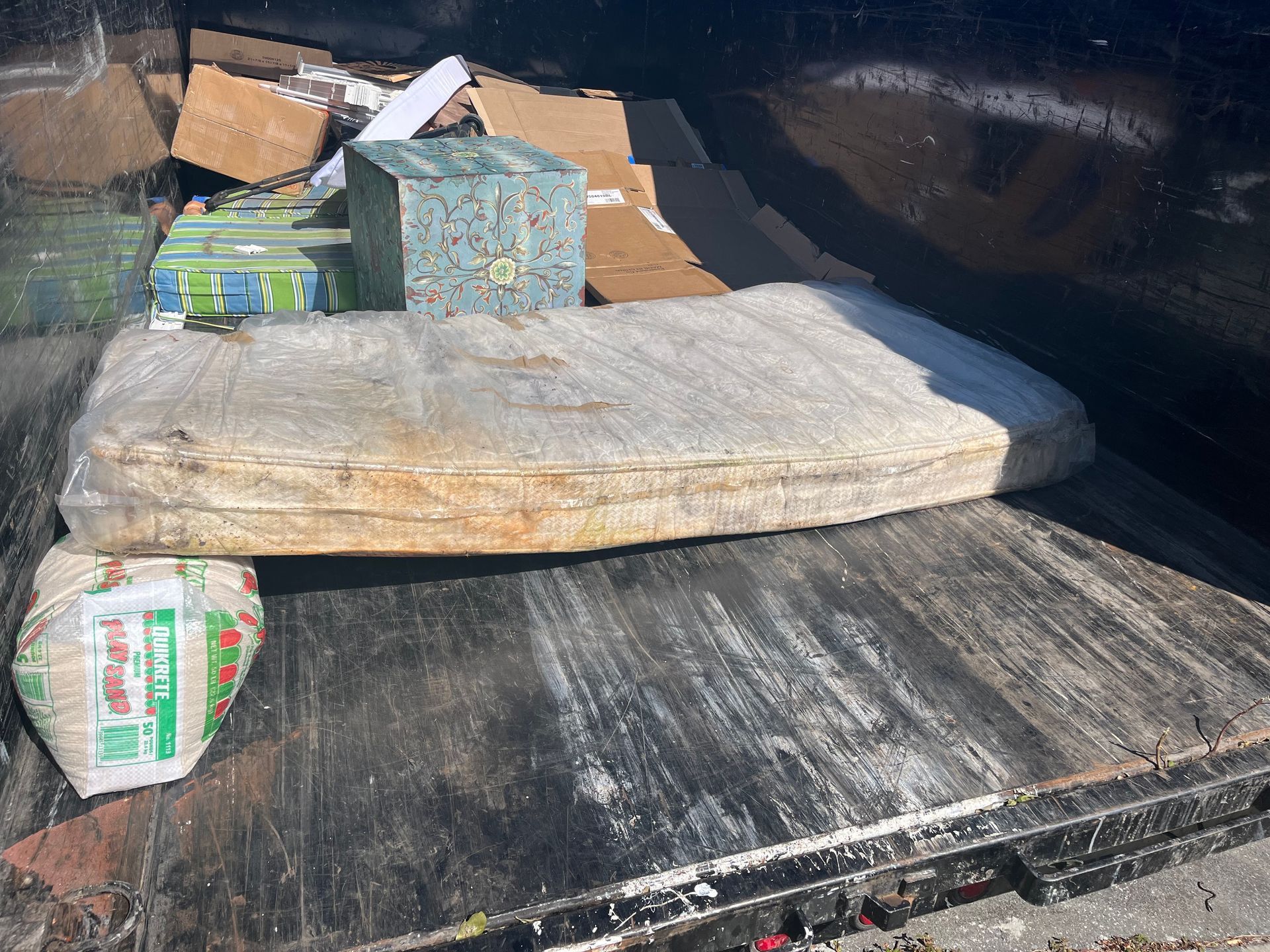 Dumpster with a mattress, boxes, and a wrapped item.