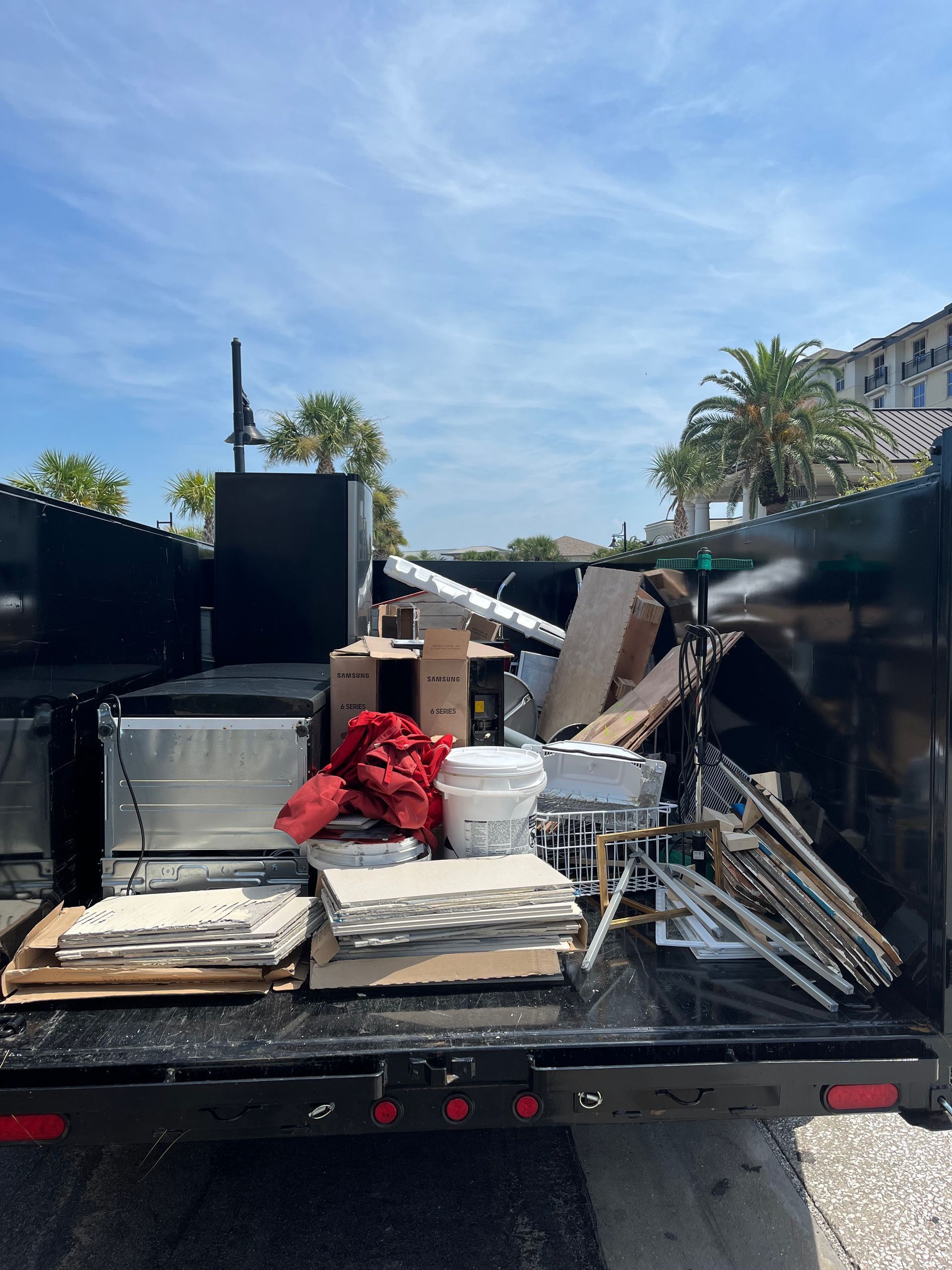 Dumpster filled with construction debris under a bright blue sky with palm trees in the background.