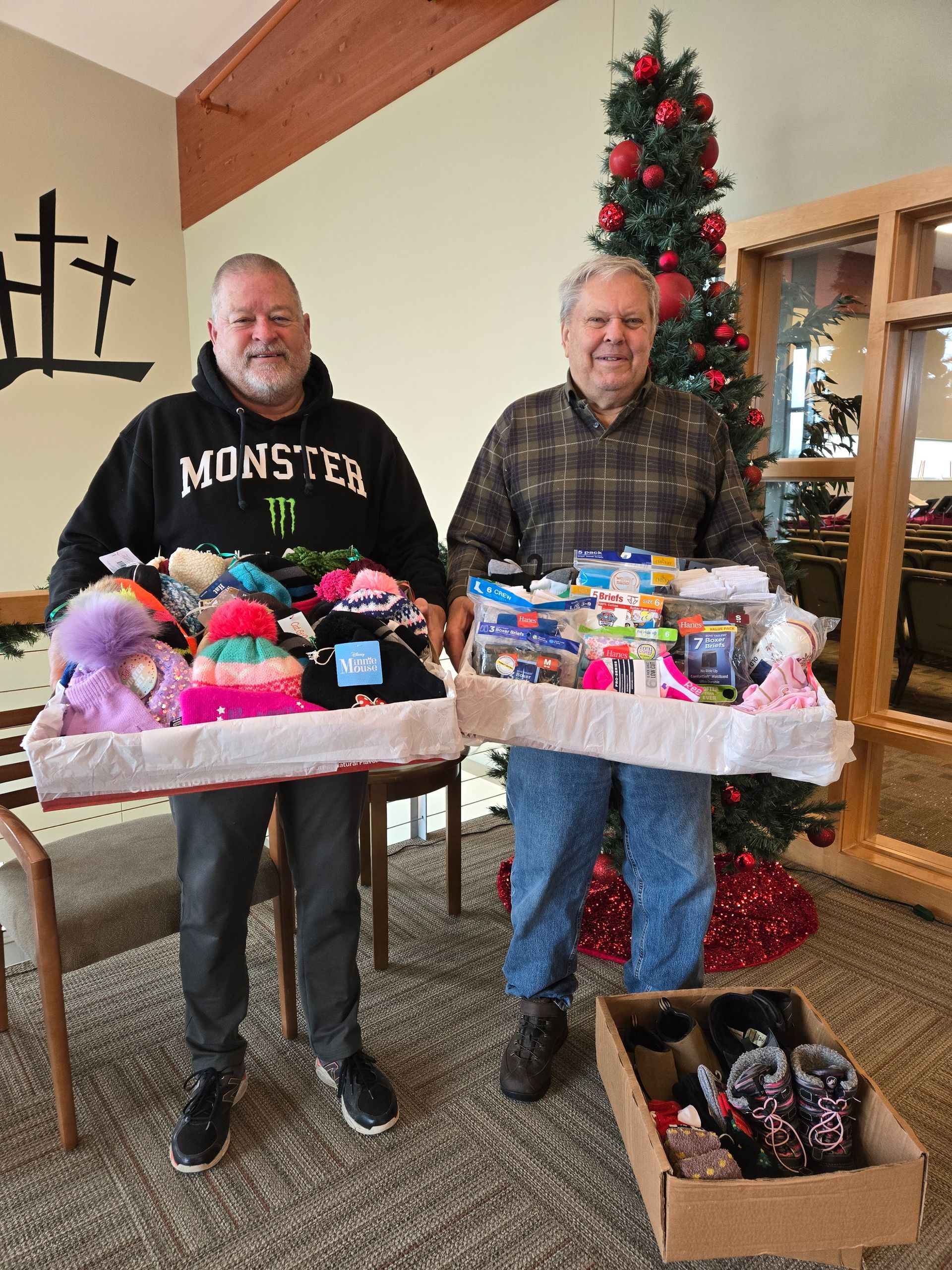 Two men holding baskets of donated items in front of a Christmas tree.