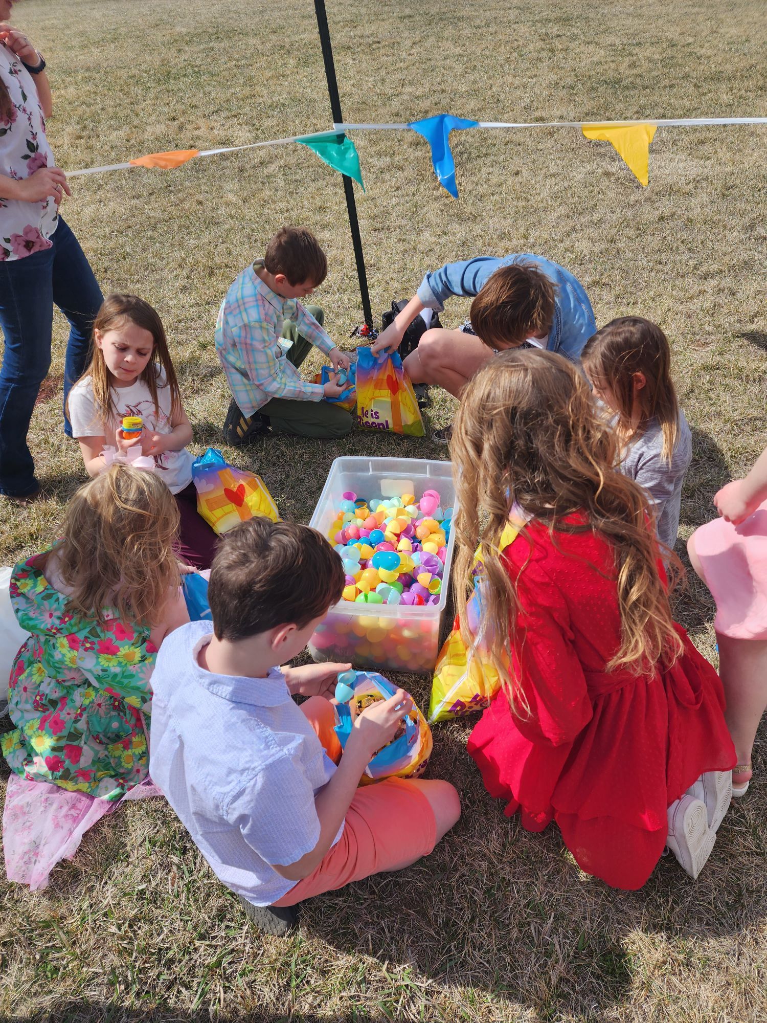 Children gather outdoors, surrounded by colorful plastic balls, likely for a game.