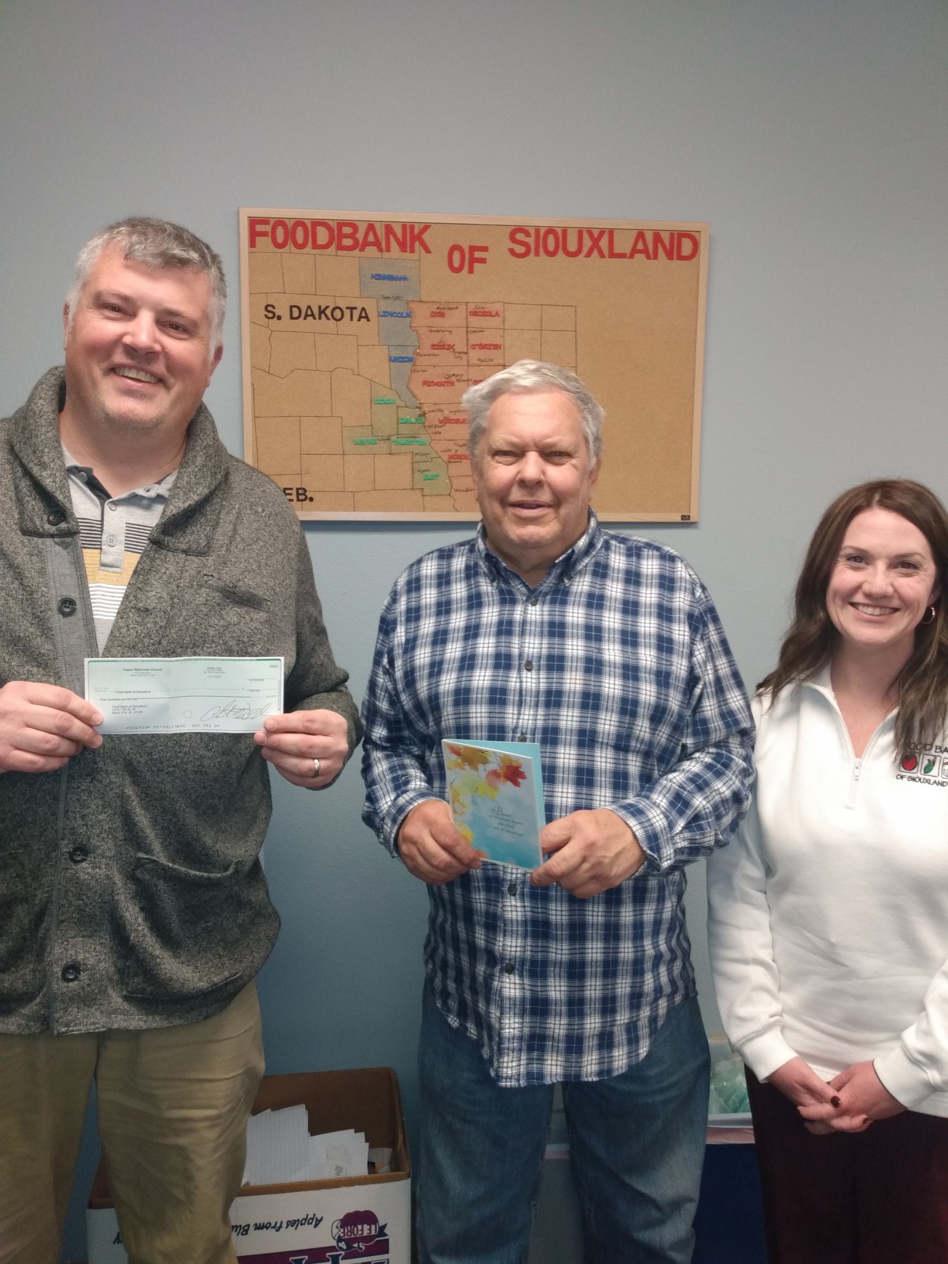 Three people at Foodbank of Siouxland: man holding a check, man with card, woman smiling; map backdrop.