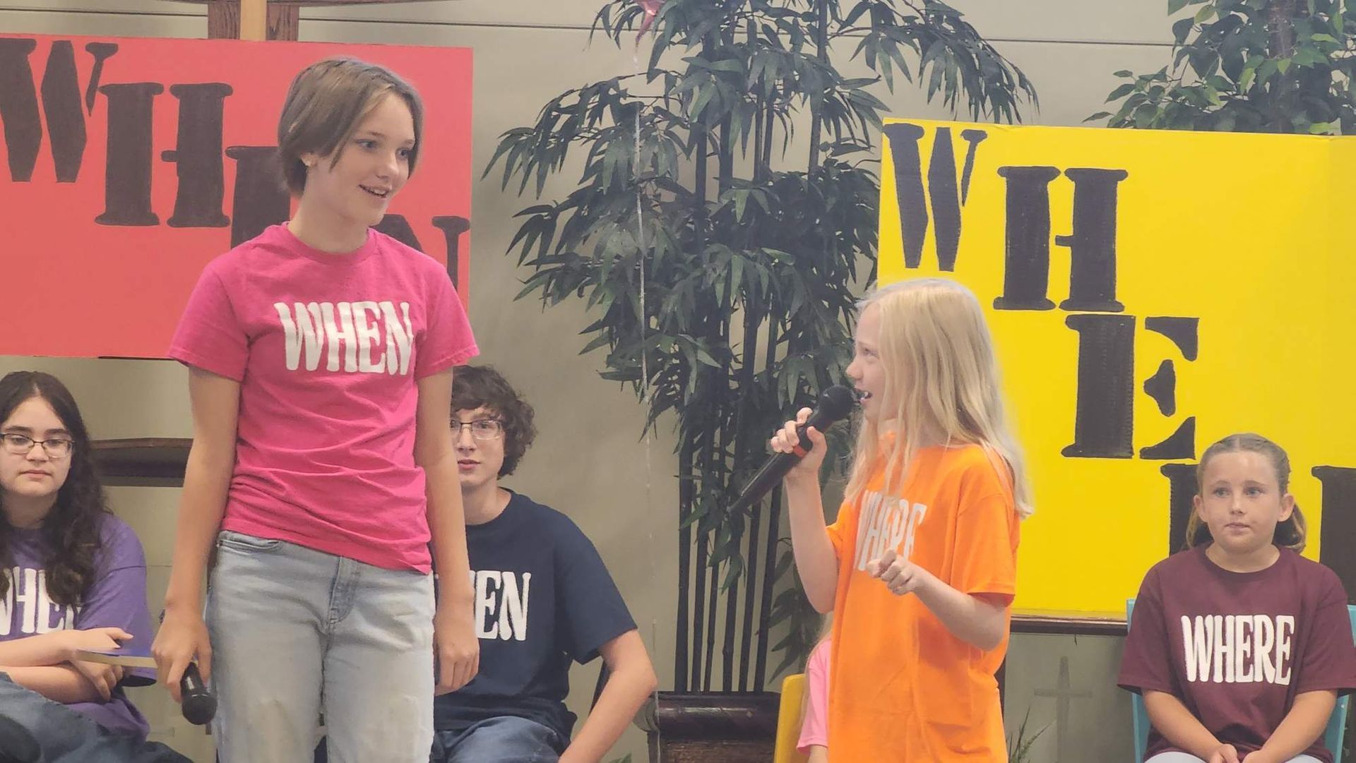Children on stage with microphones, in front of 