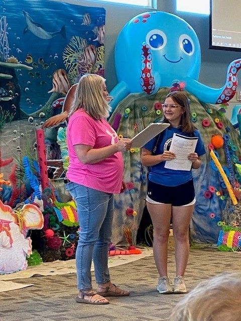 Two people stand in front of an underwater-themed display, one holding a clipboard, another with papers.
