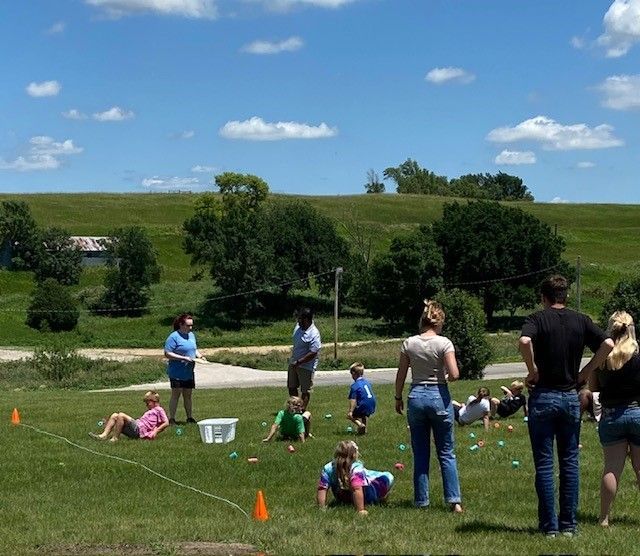 People playing an outdoor game on grass, with adults and children. Hills and blue sky in the background.