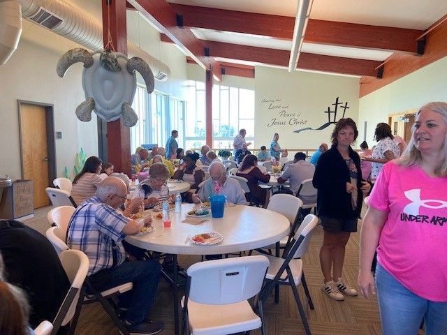 People eating at round tables in a brightly lit room, with a turtle decoration hanging from the ceiling.