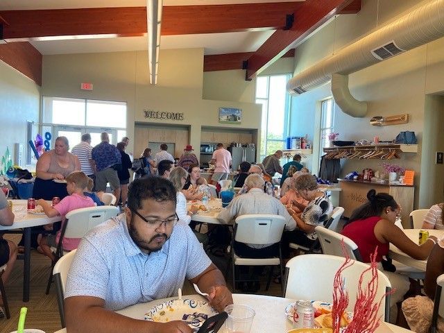People seated at tables in a community room, eating and socializing. 