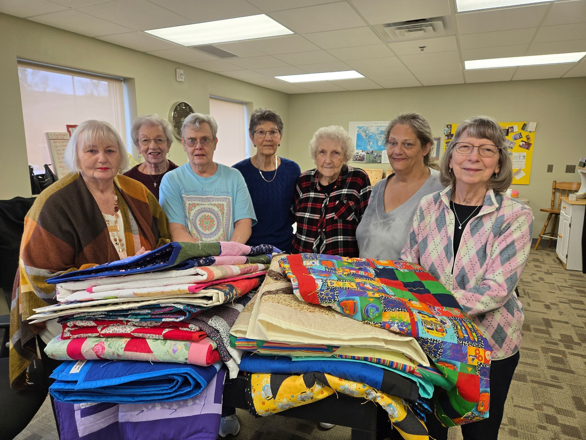 Group of people holding quilts in a brightly lit room.