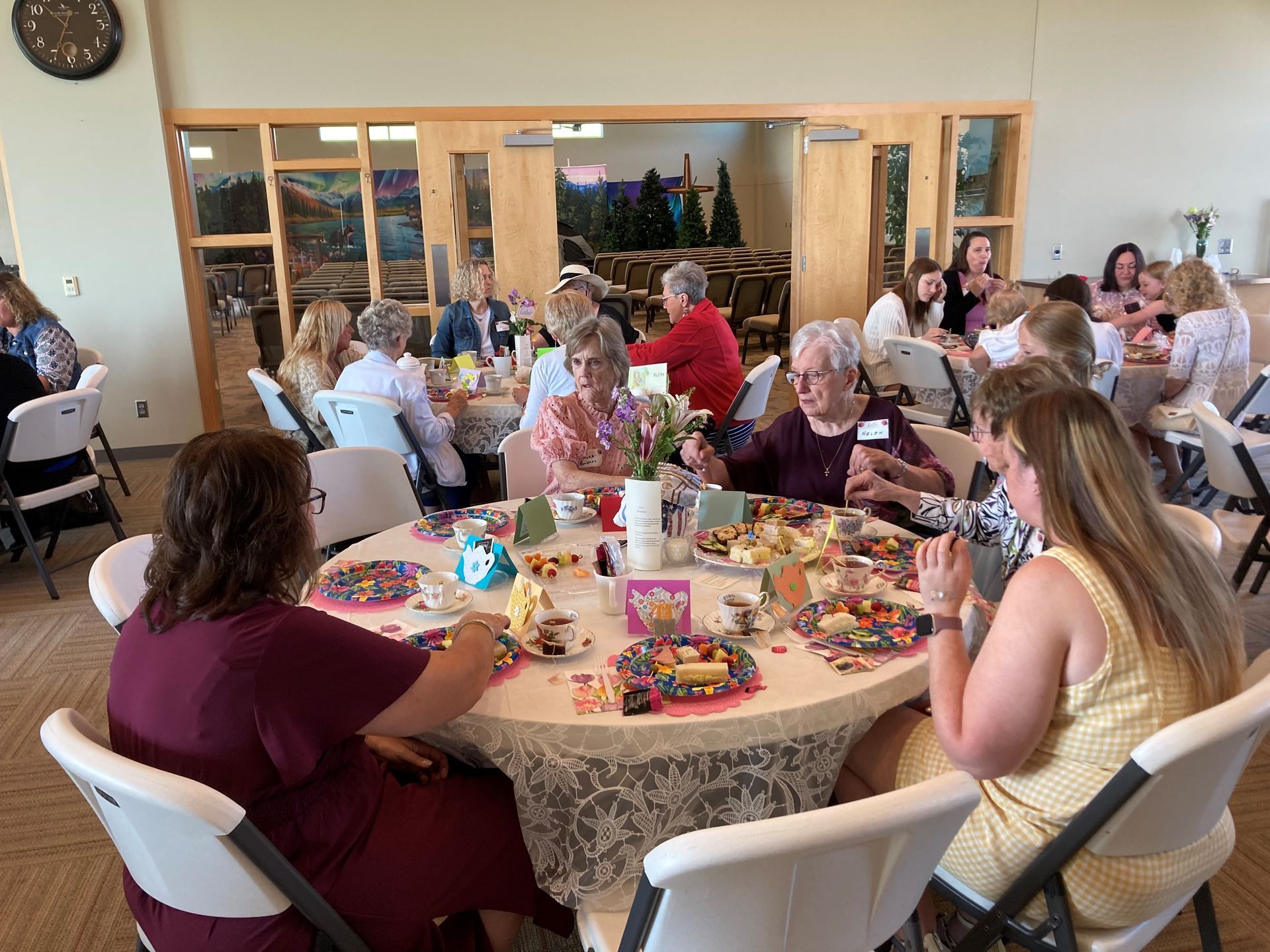 People seated around tables in a brightly lit room, engaged in conversation and activities.