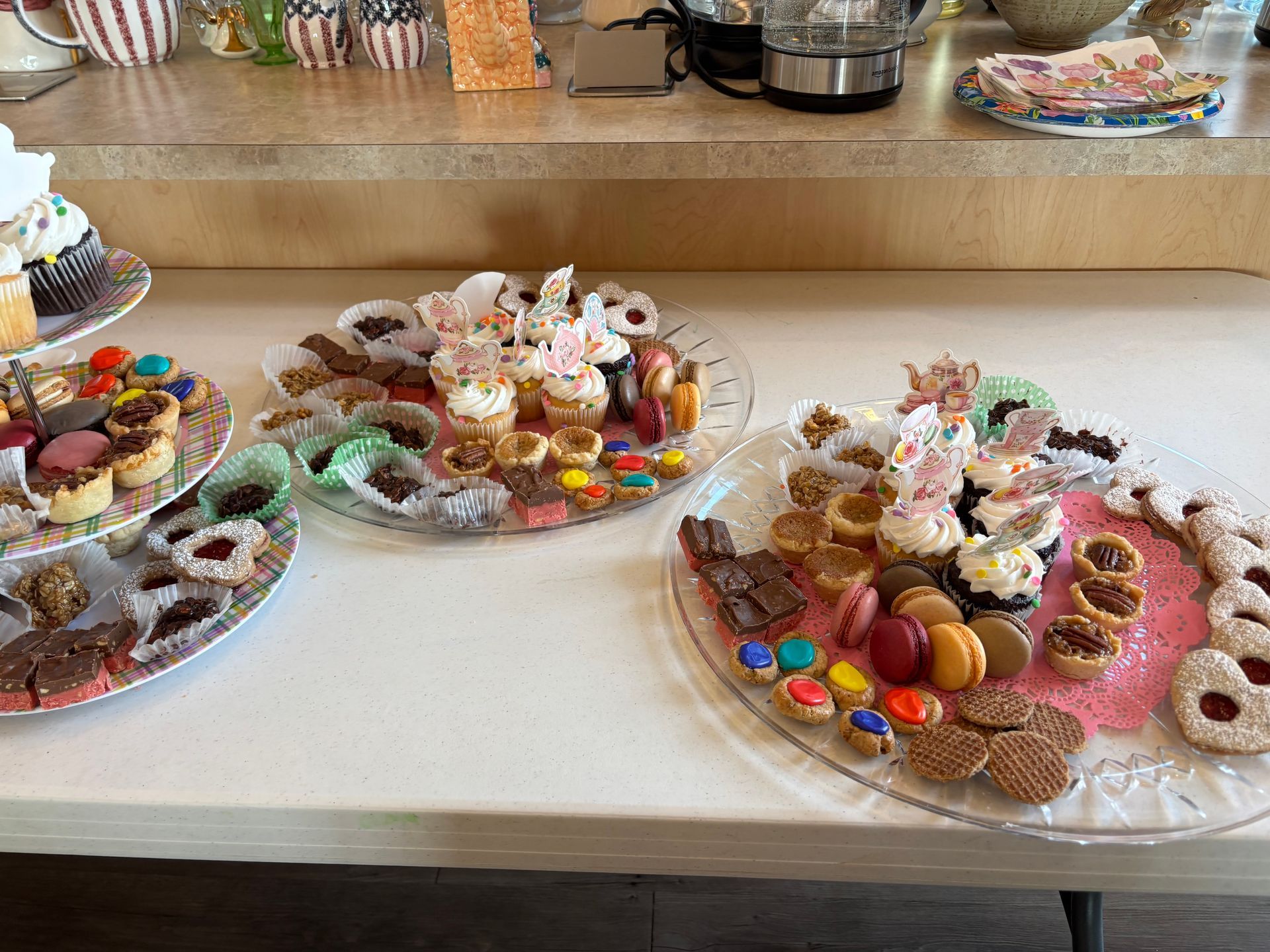 Dessert table with various cookies, cupcakes, and candies arranged on clear plates.