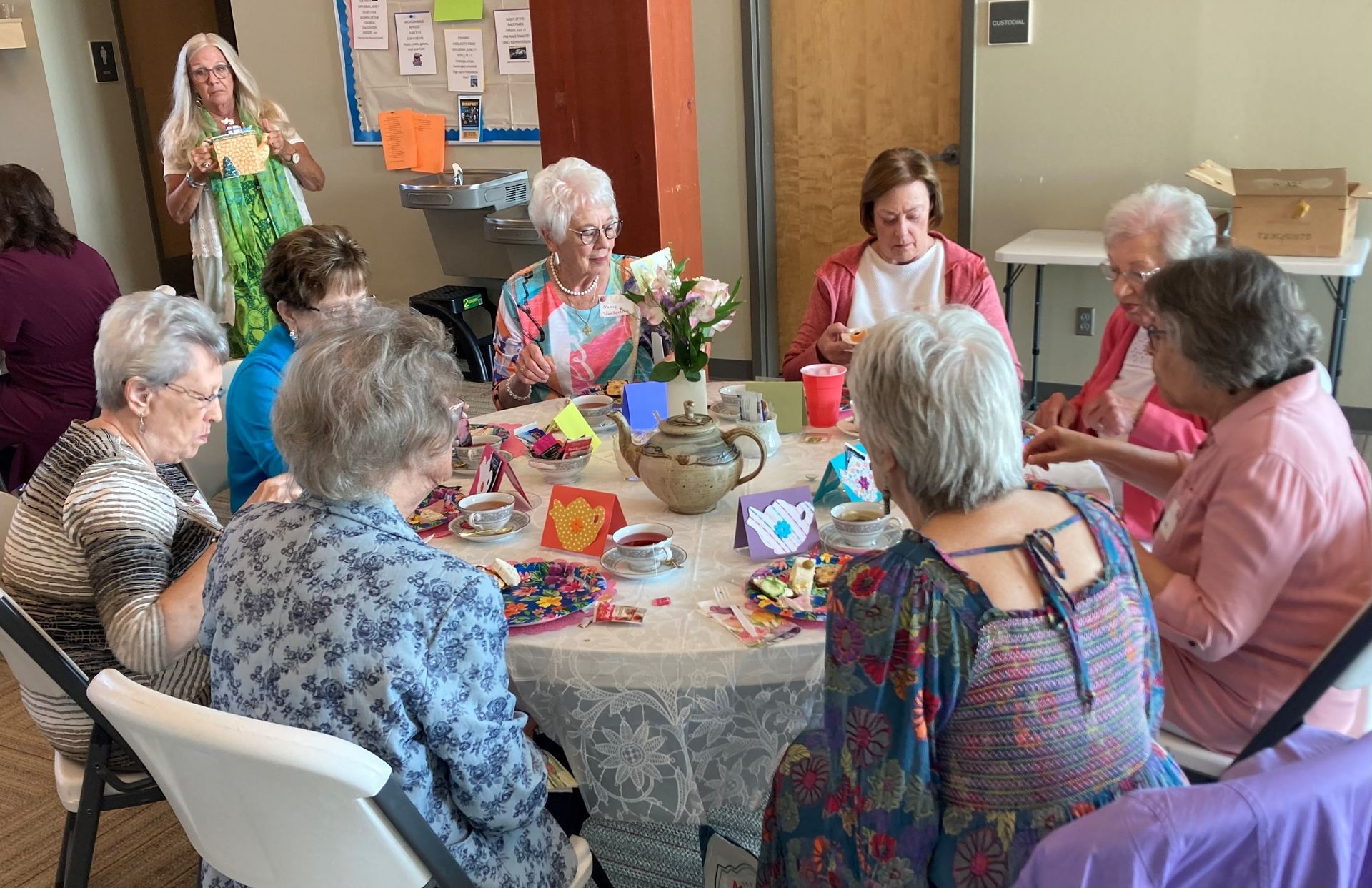 A group of women crafting around a table; flowers, paper, and supplies are present.