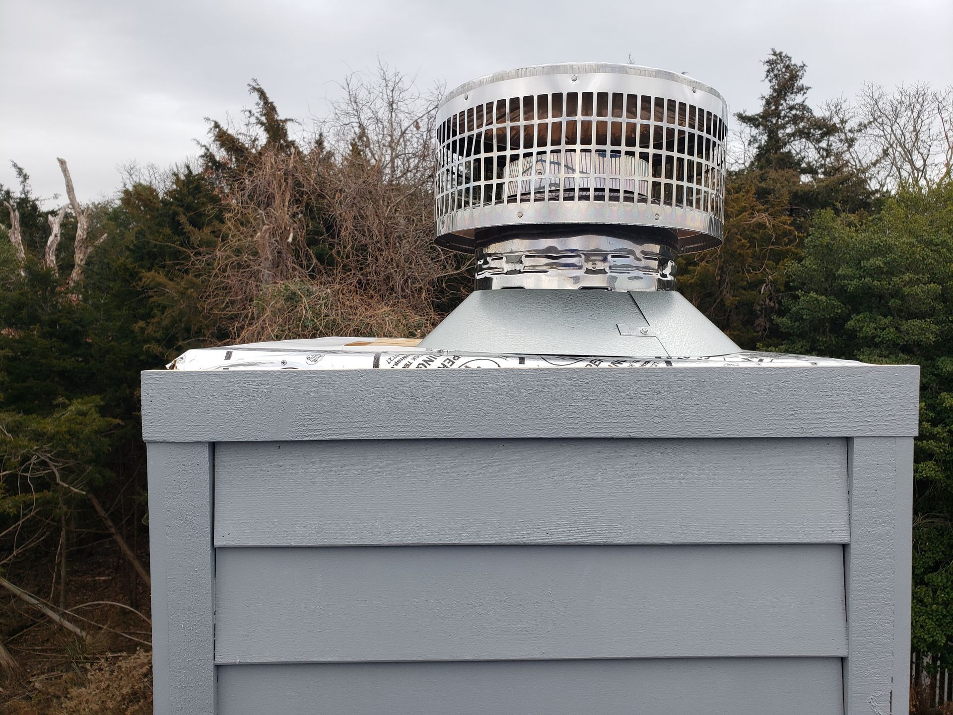Rooftop ventilation unit with a gray housing against trees and cloudy sky
