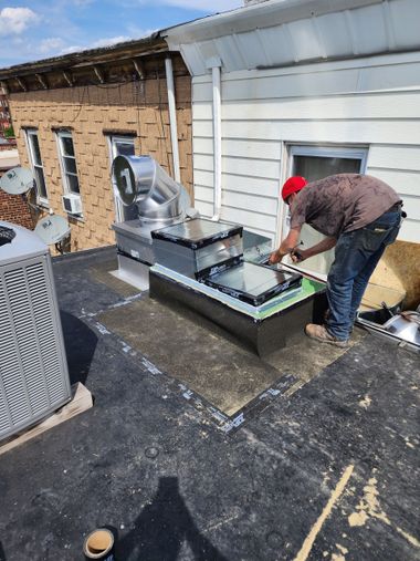 Worker installing rooftop HVAC unit on a flat roof beside a white building