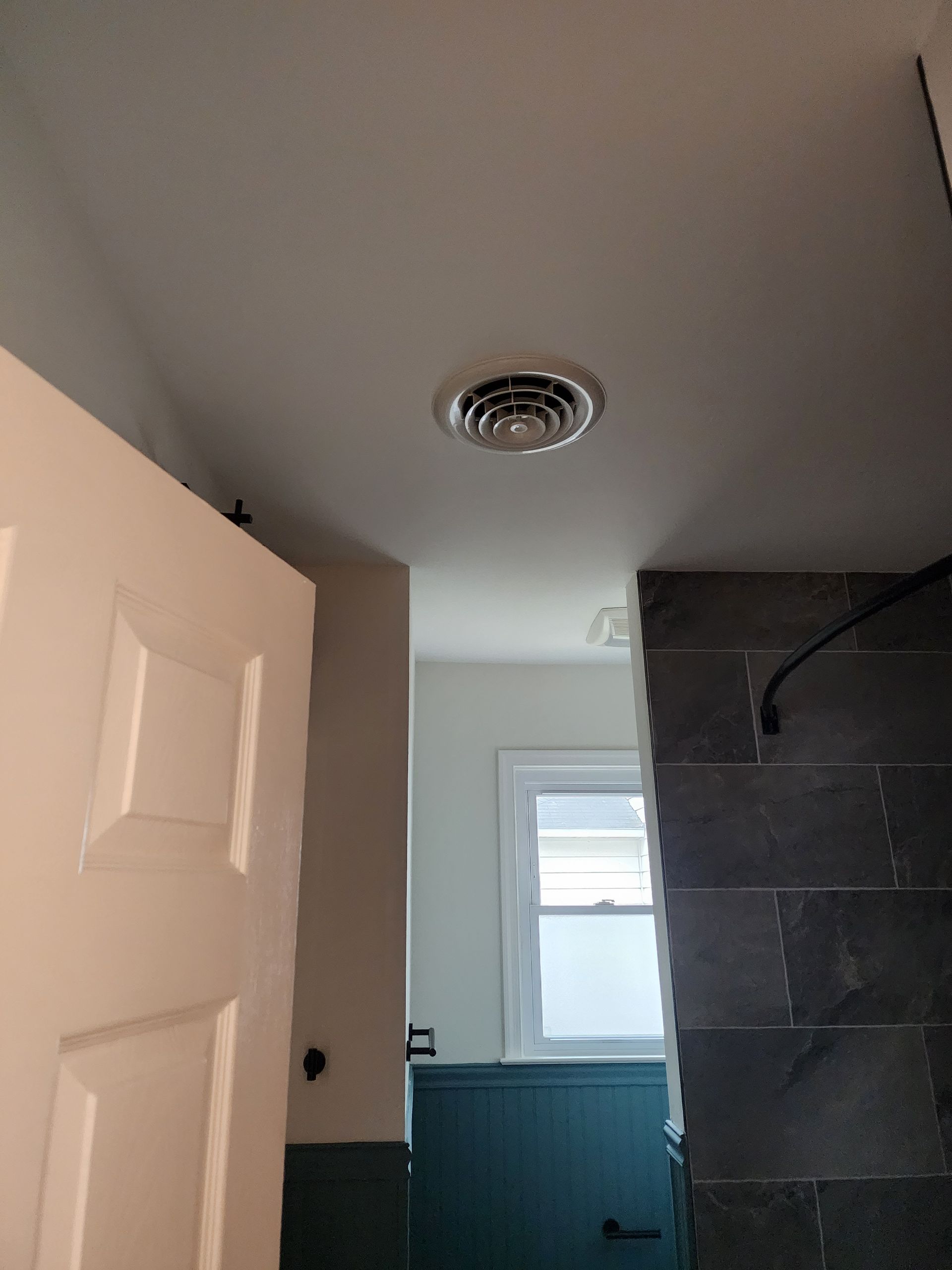 Bathroom with open white door, ceiling vent, window, teal wall tiles, and dark shower wall tiles