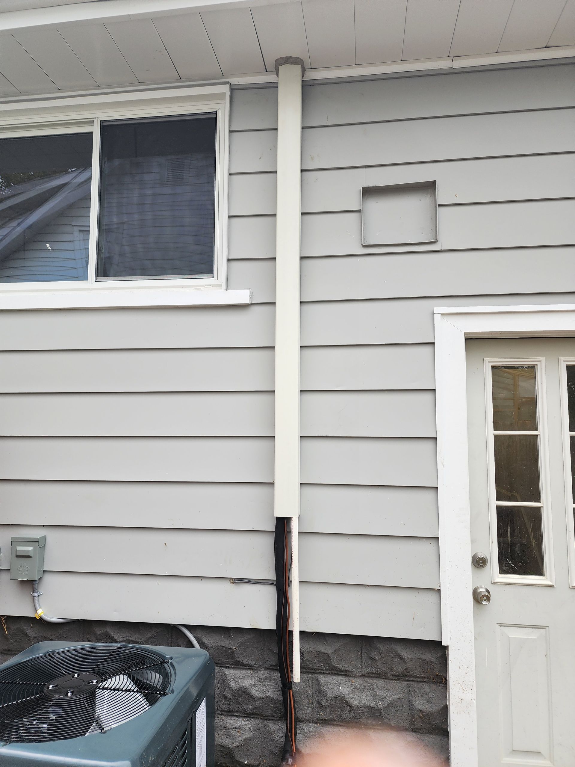 House exterior with gray siding, a white door, and a damaged downspout near the foundation