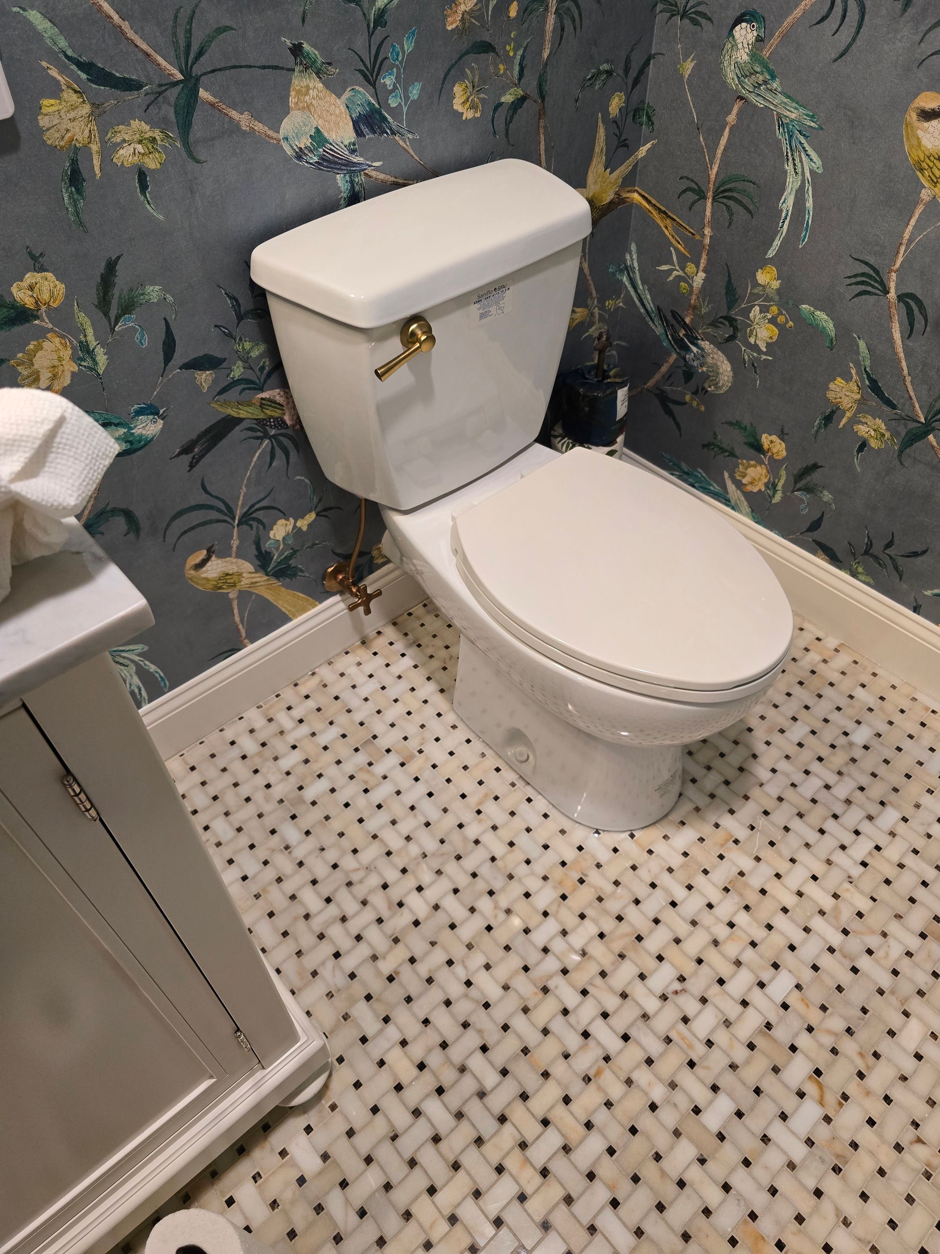 Small bathroom with a white toilet, patterned wallpaper, and mosaic tile floor.
