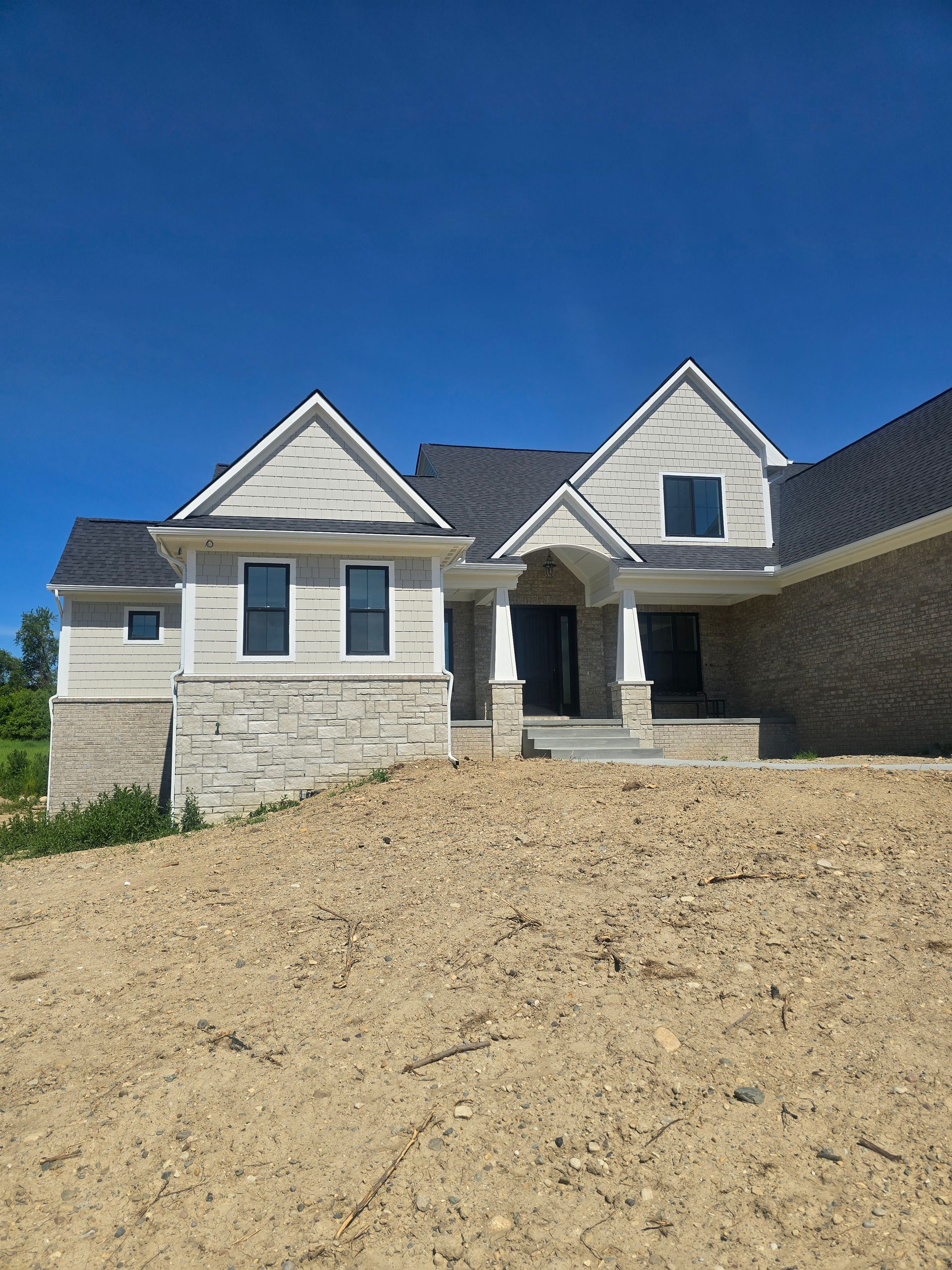 New beige stone house under construction with blue sky and bare dirt foreground