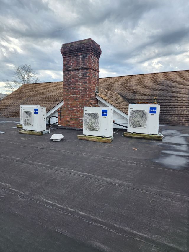 Three rooftop HVAC units beside a brick chimney under a cloudy sky
