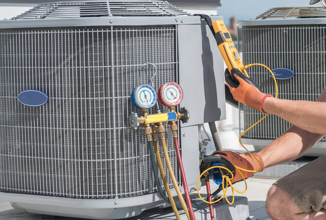 Technician using gauges and a vacuum pump to service an HVAC condenser unit outdoors