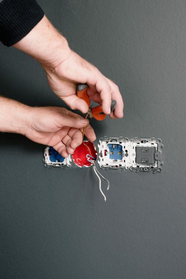 Hands wiring an exposed wall outlet with red and blue electrical components