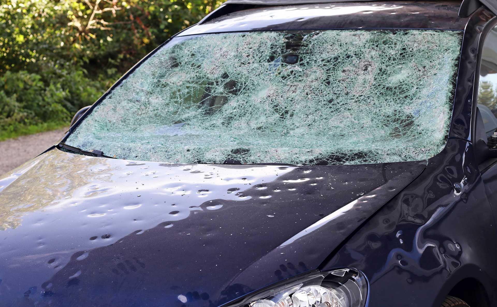 A car with a broken windshield is parked on the side of the road