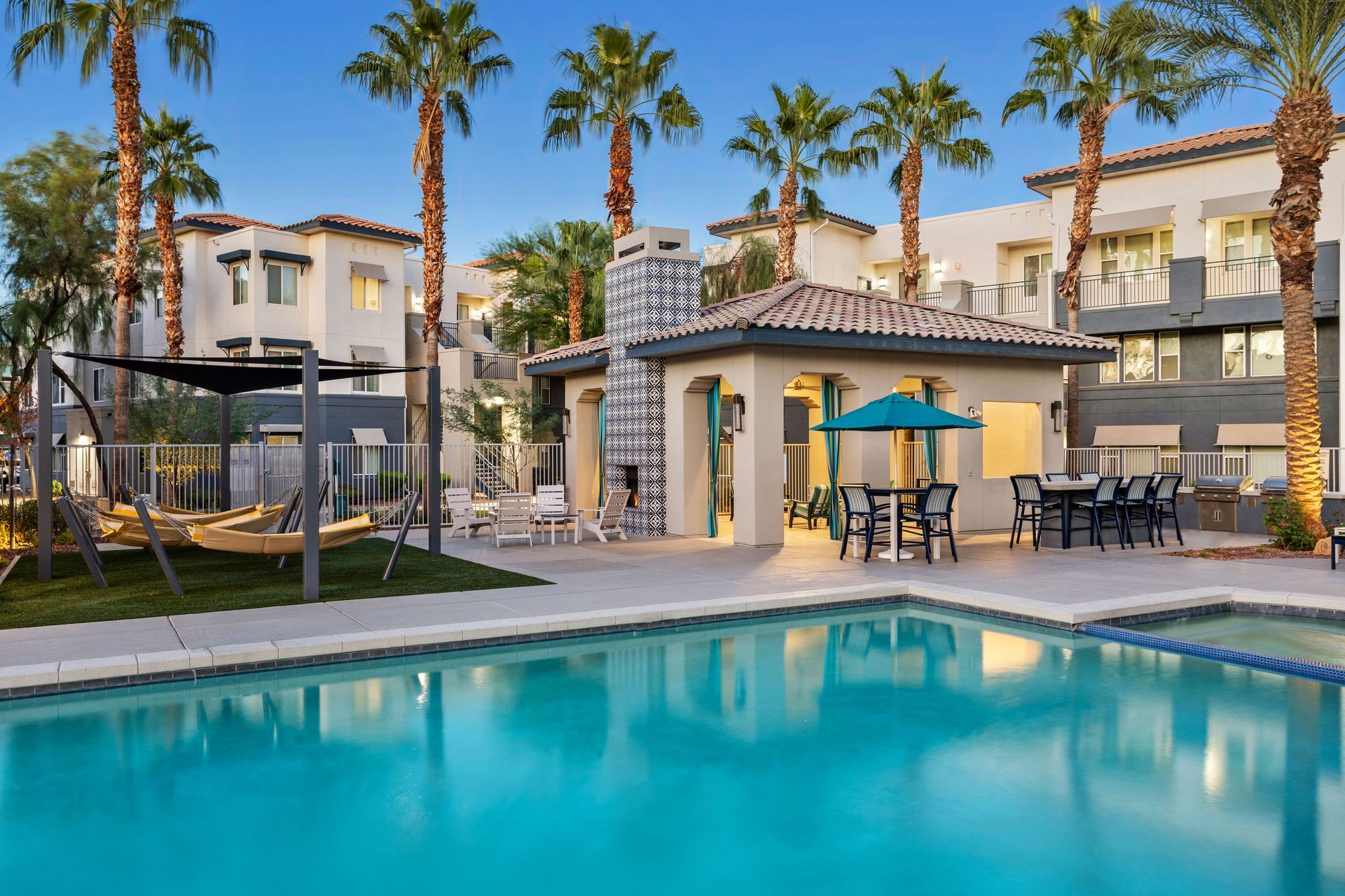 Pool area with buildings, palm trees, and outdoor seating. Turquoise water and a sunny day.