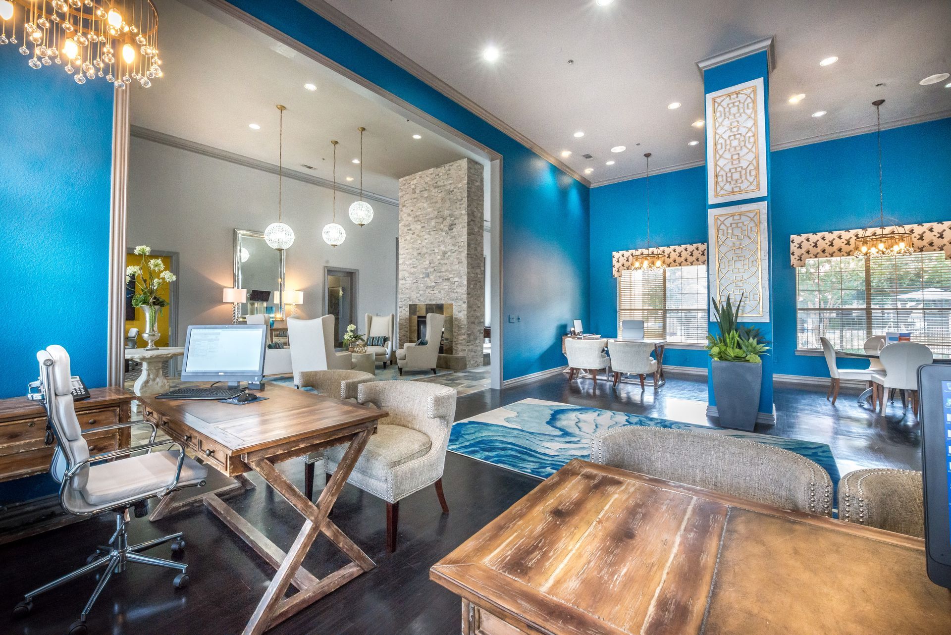 Spacious lobby with blue walls, wooden tables, and seating areas. Brightly lit with multiple light fixtures.