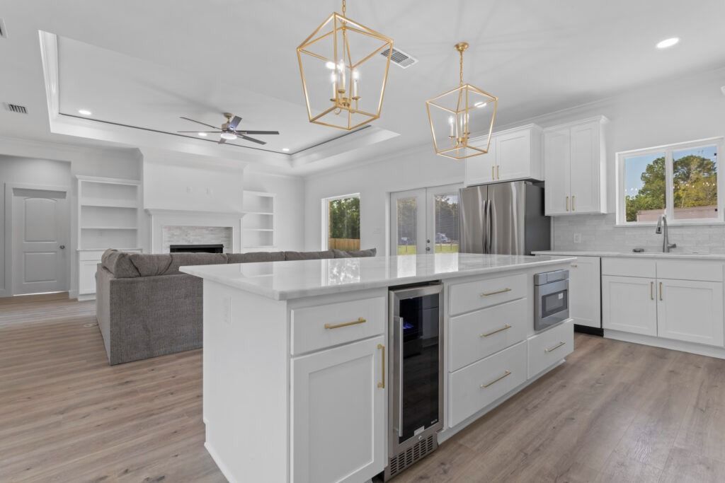 Modern kitchen with white cabinets, island, stainless steel appliances, and gold light fixtures.