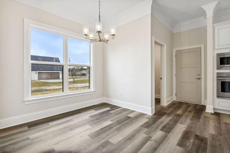 Dining room with large window, chandelier, and wood-look flooring. Neutral walls and trim.