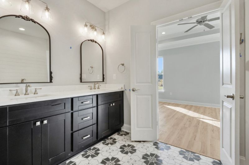 Bathroom with black vanity, floral tile, and doorway to a bedroom with a ceiling fan.
