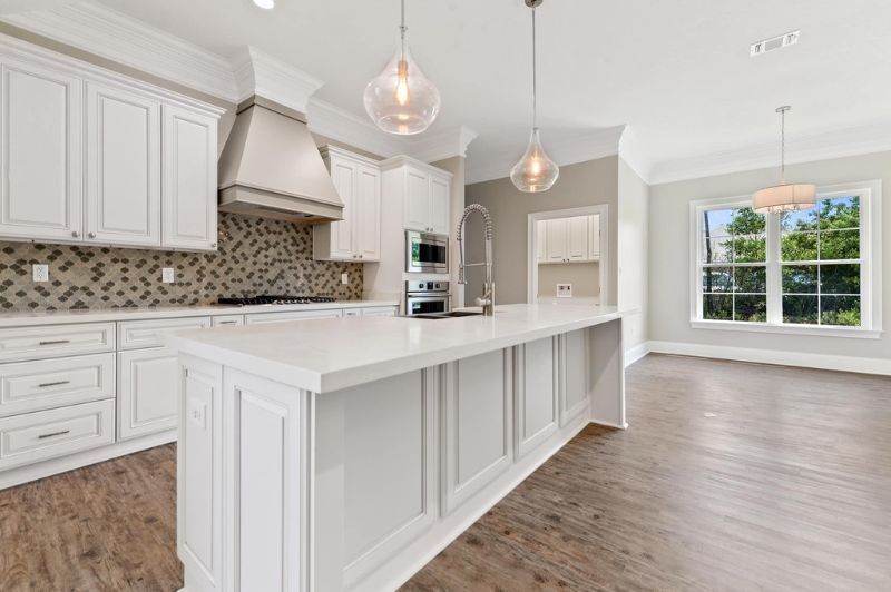 Modern white kitchen with island, light wood floors, and two pendant lights.